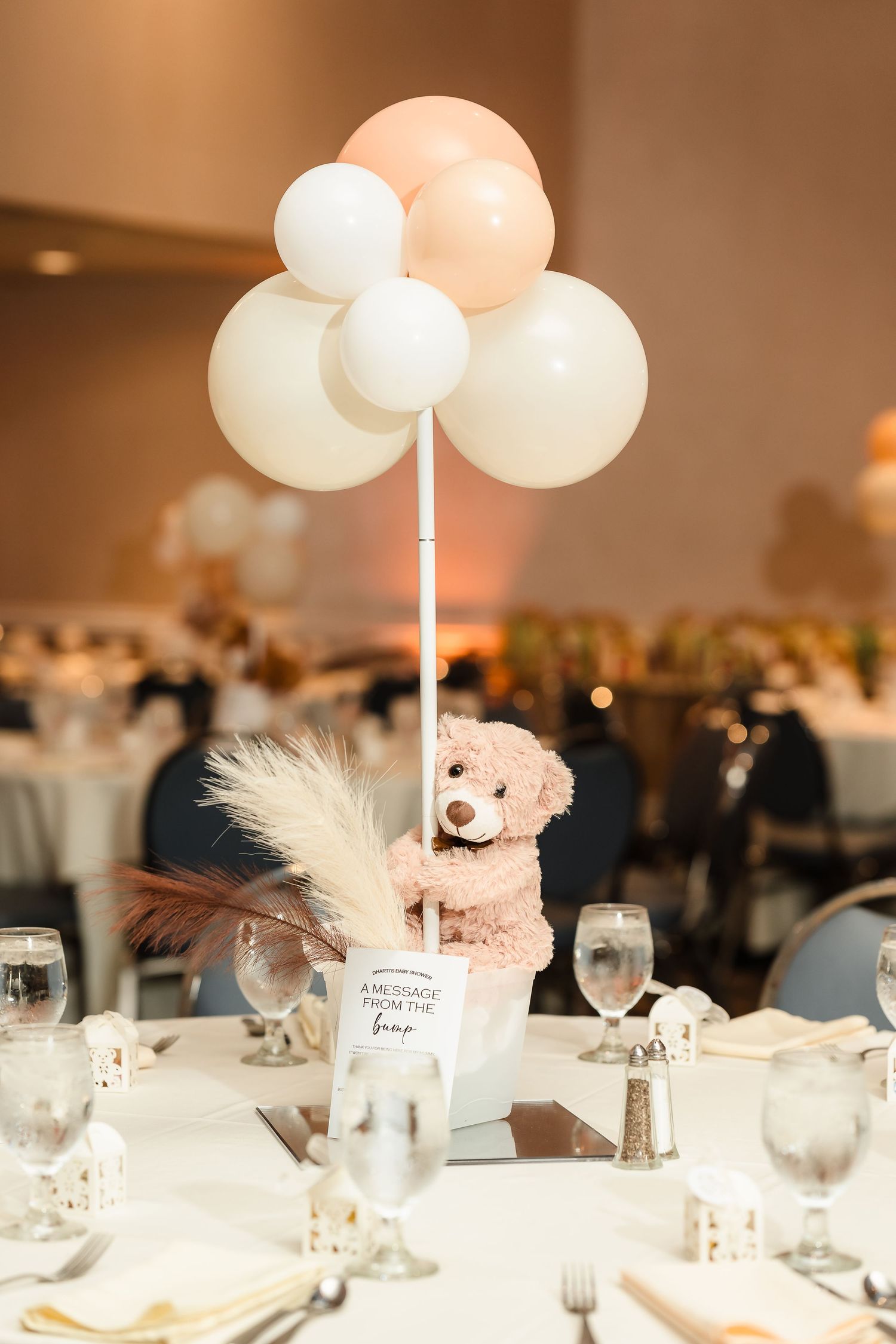 Pink and white balloons with a teddy bear centerpiece for a baby shower table decoration.