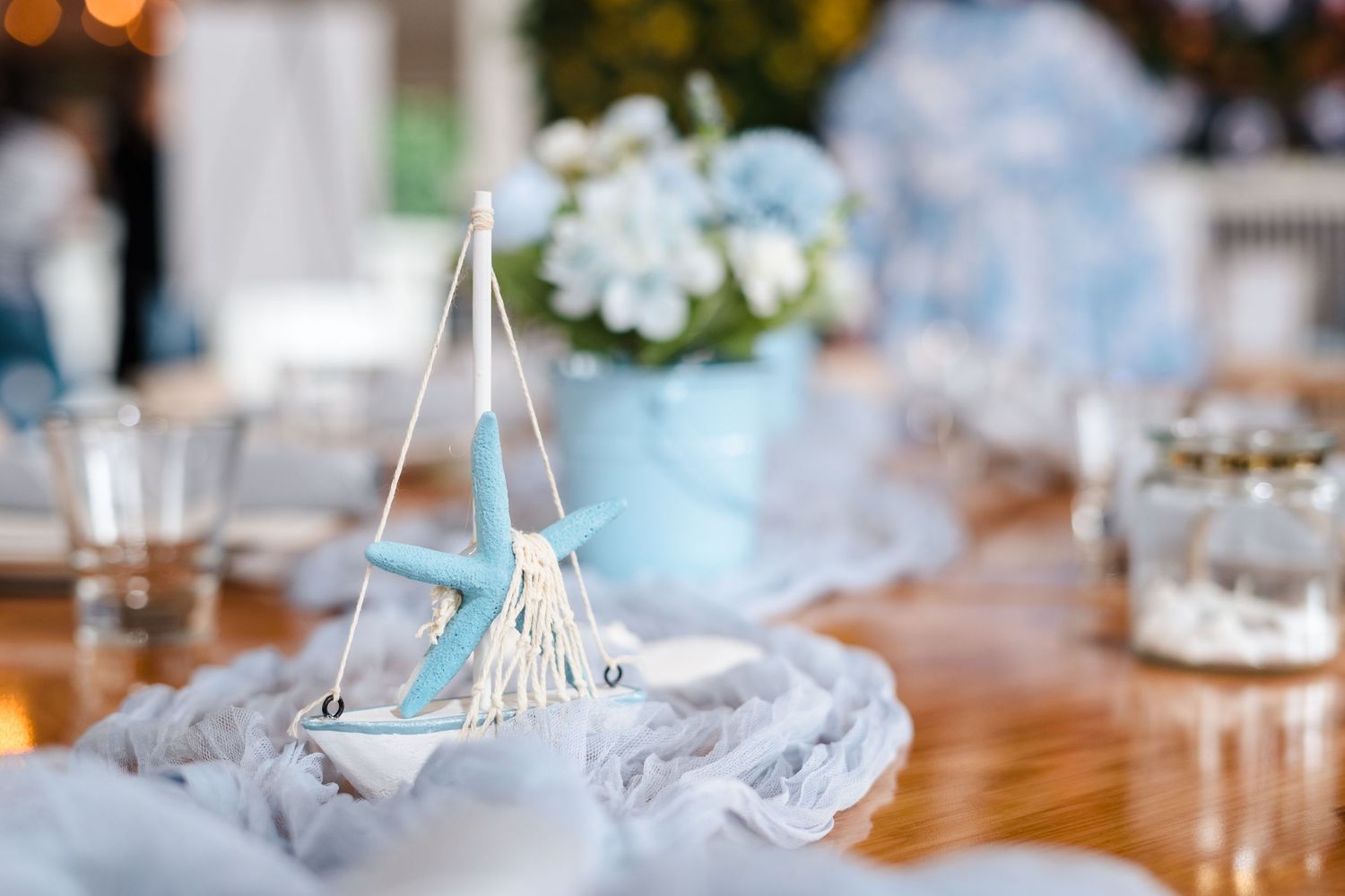 Glass pyramid-shaped terrarium with white feather on wooden table among dreamy blue and white table decor.