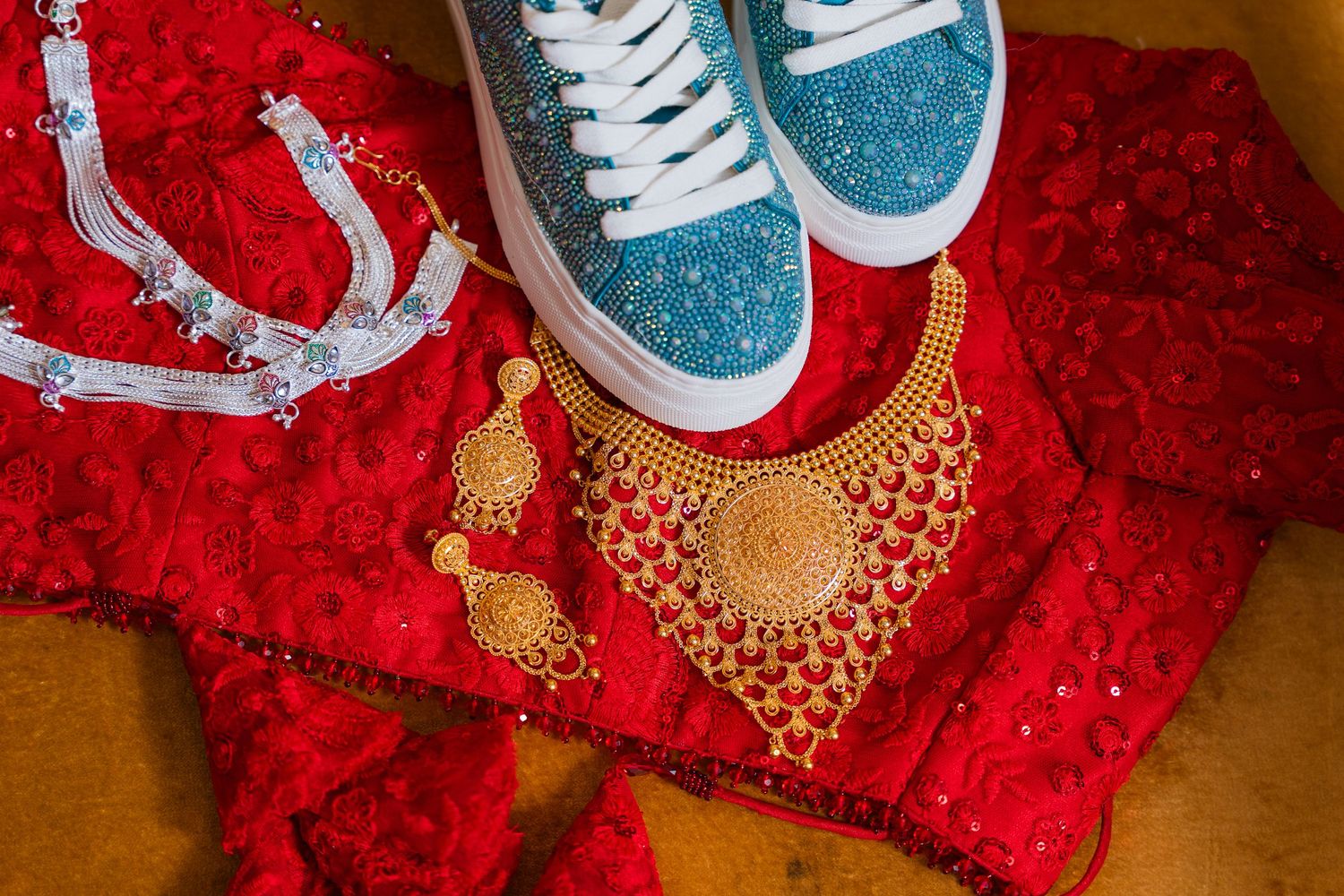 Sparkly blue sneakers and gold jewelry arranged on red fabric.