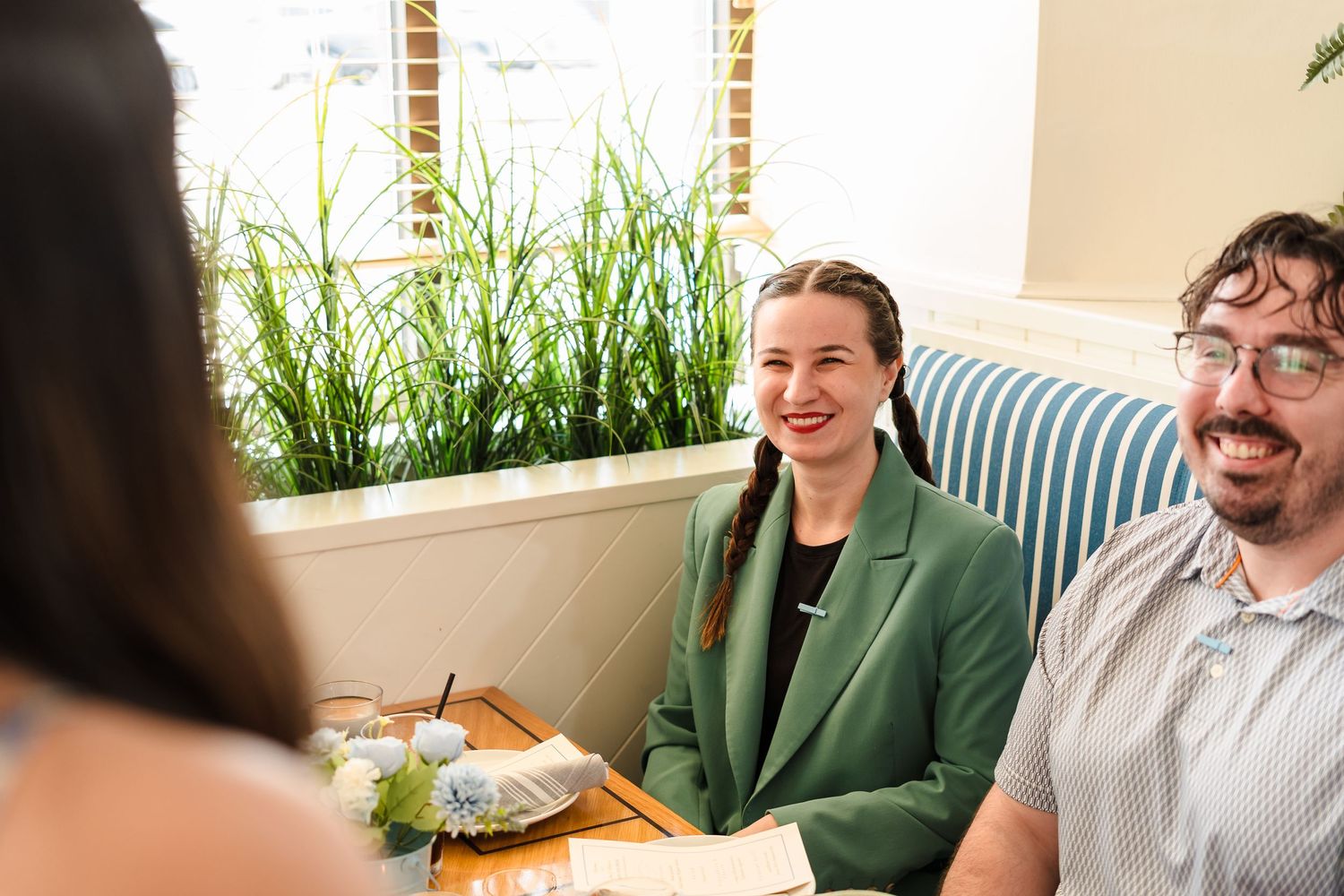 People enjoying a casual dining experience at a restaurant with greenery and natural lighting.