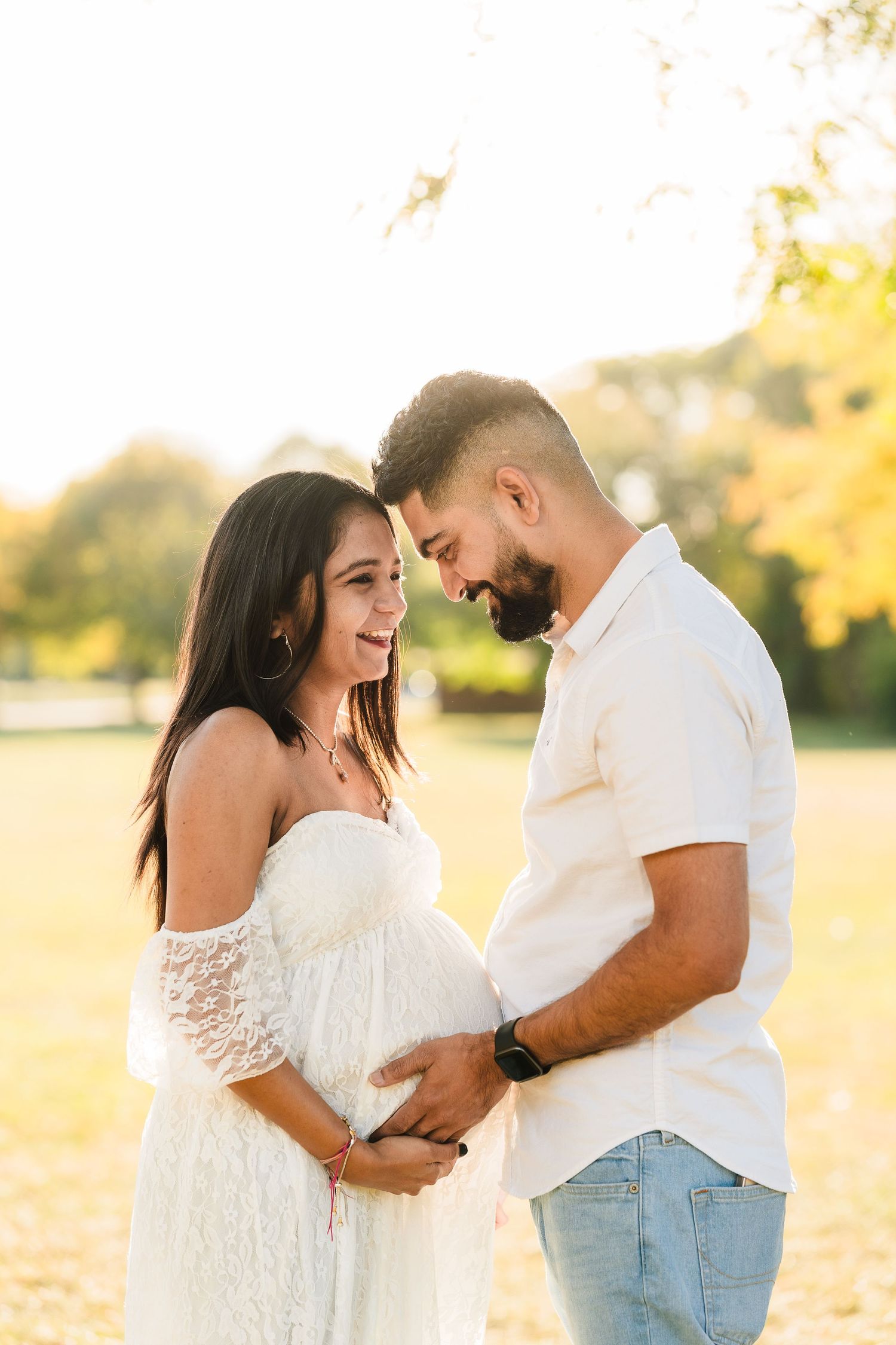 Couple shares tender moment during sunset maternity photoshoot outdoors.