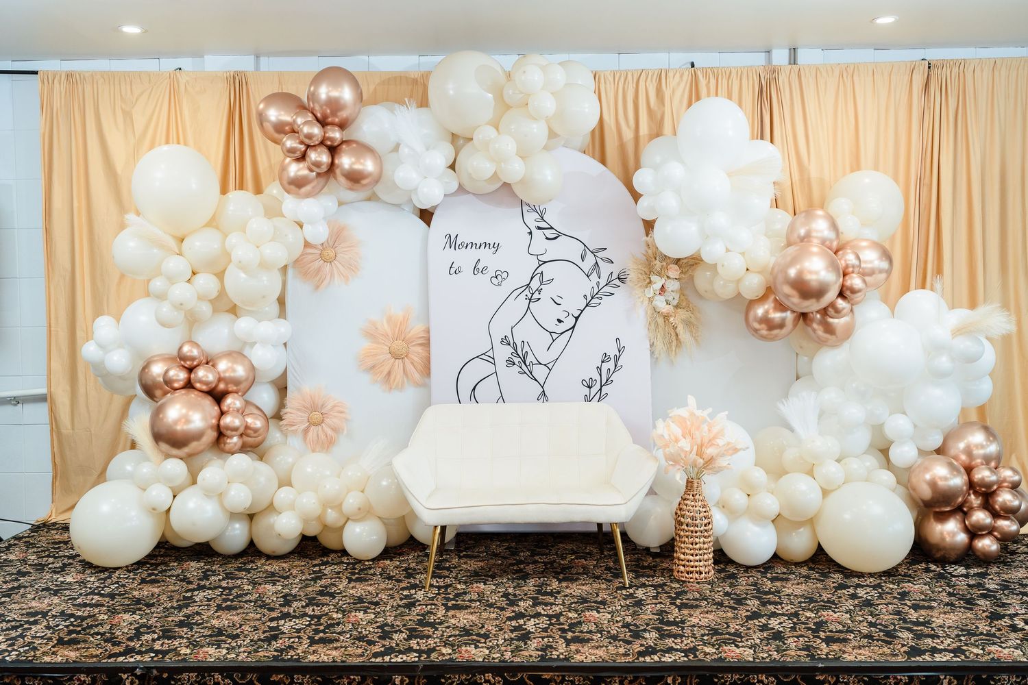 Baby shower backdrop with white and rose gold balloon garland surrounding a white chair.