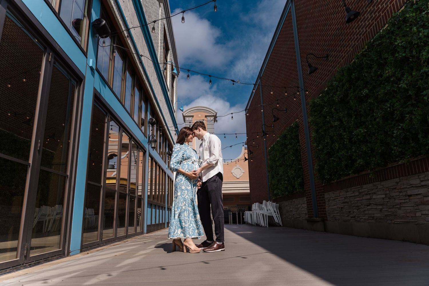 A couple embraces next to a modern building with blue trim and brick walls on a sunny afternoon.