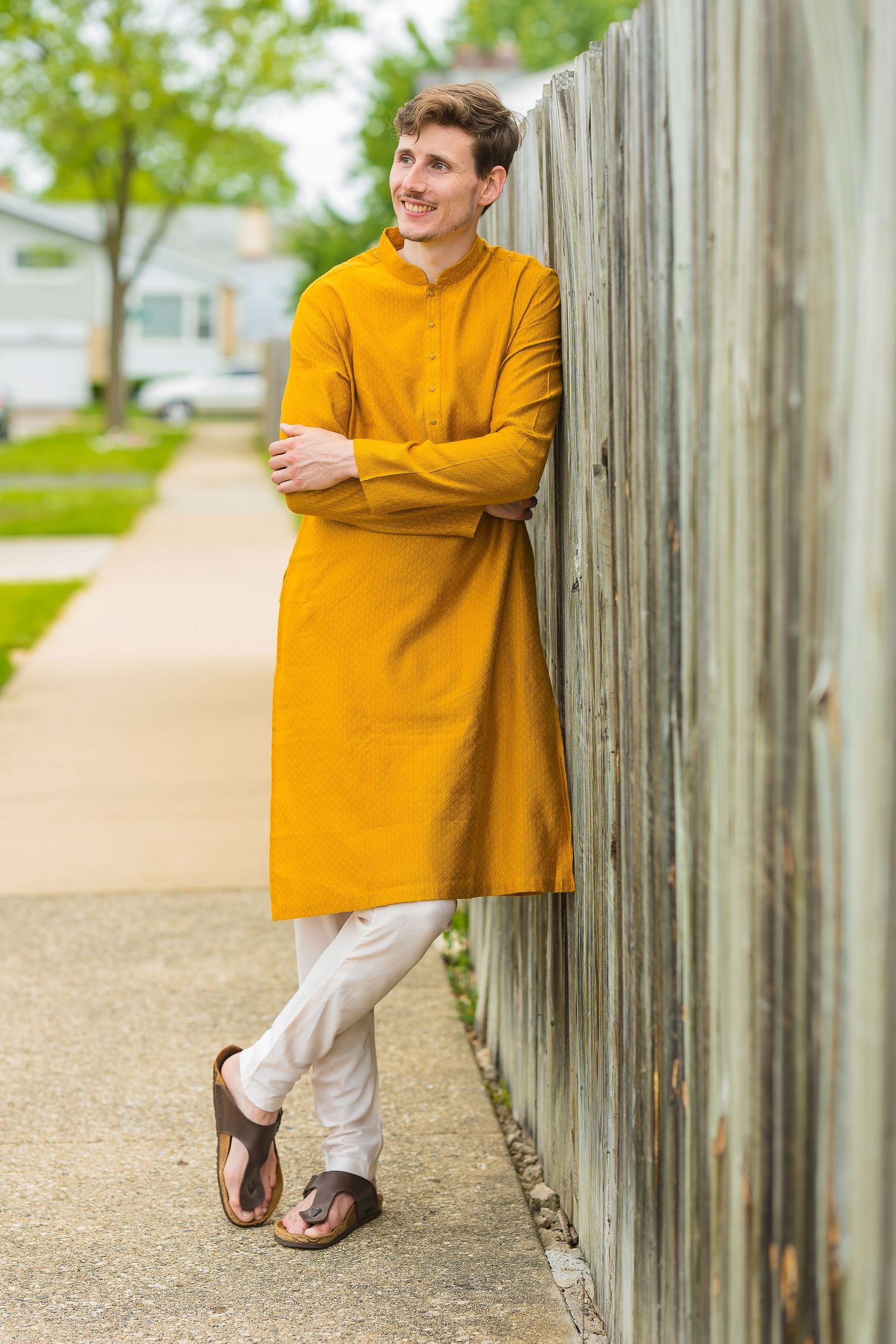 Person in mustard yellow kurta leaning against wooden fence in casual pose.