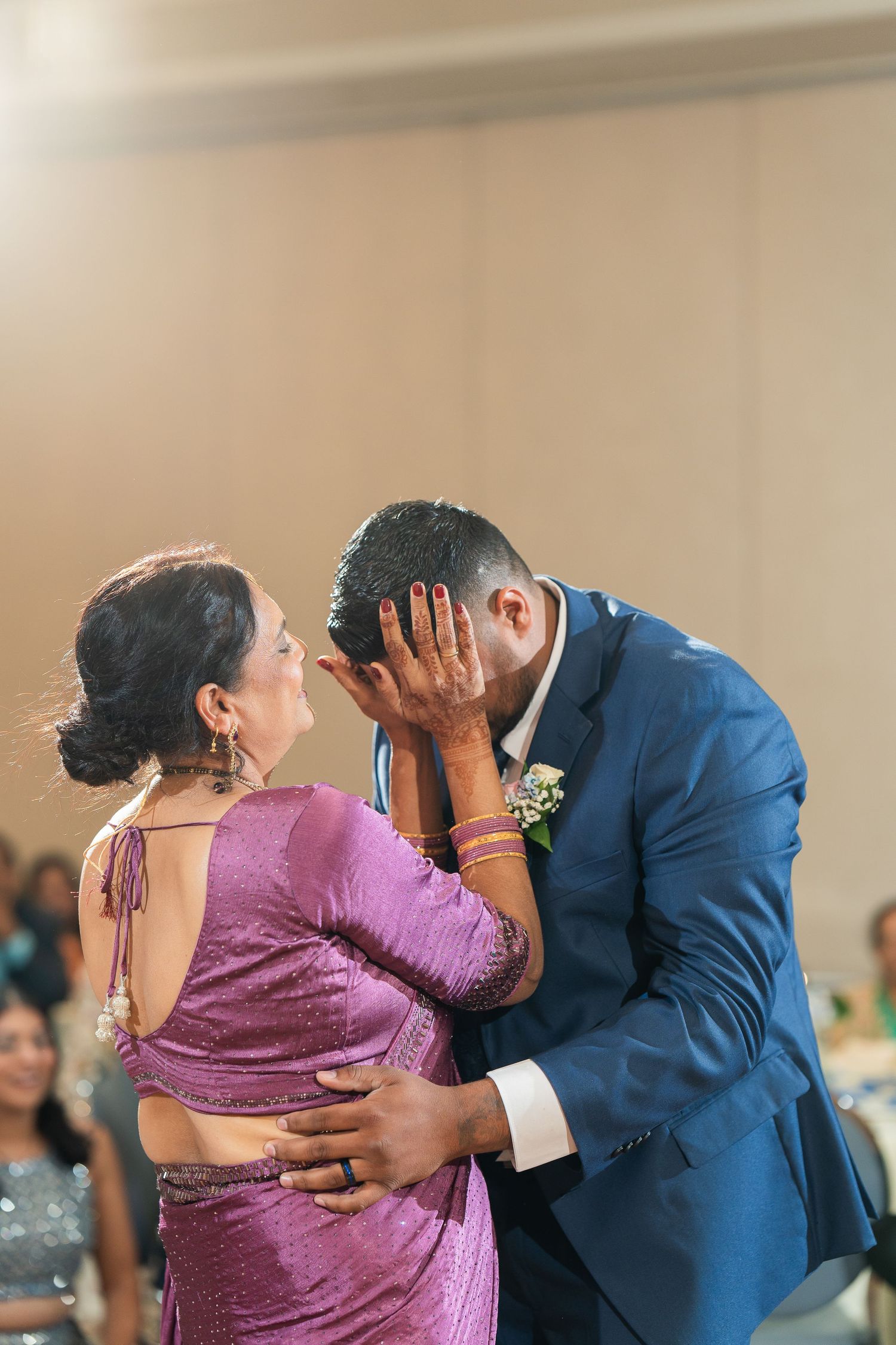 A tender moment shared during a dance, with a person in a purple sari and another in a navy blue suit embracing.