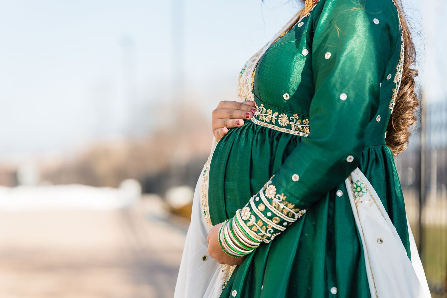 Close-up of emerald green traditional Indian dress with gold bangles and embellishments.