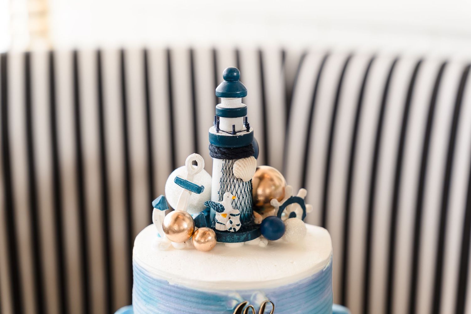A white and navy blue nautical themed wedding cake topper decorated with seashells and a striped lighthouse ornament.