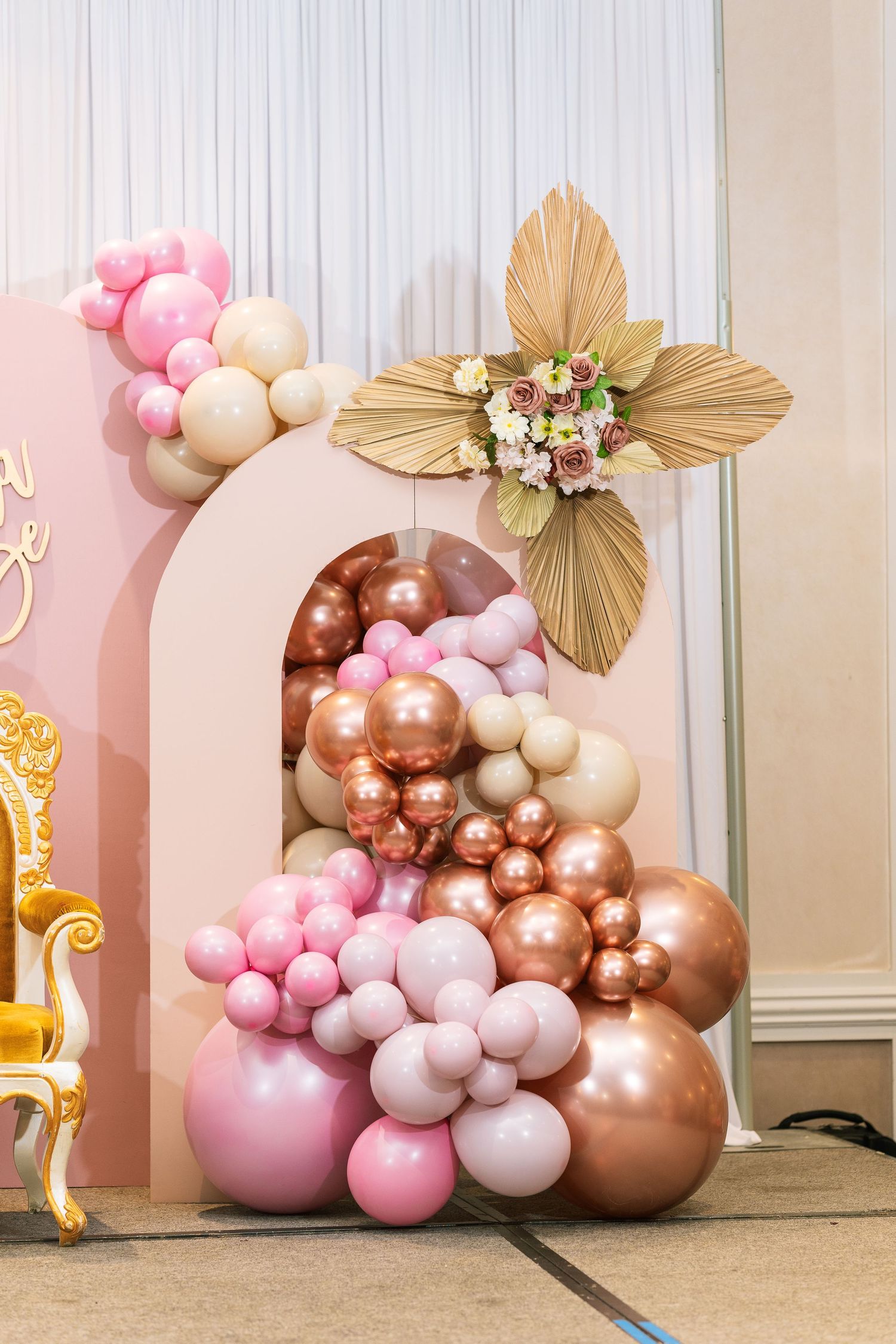 Pink and gold balloon arch with metallic decorations and a golden leaf accent piece.