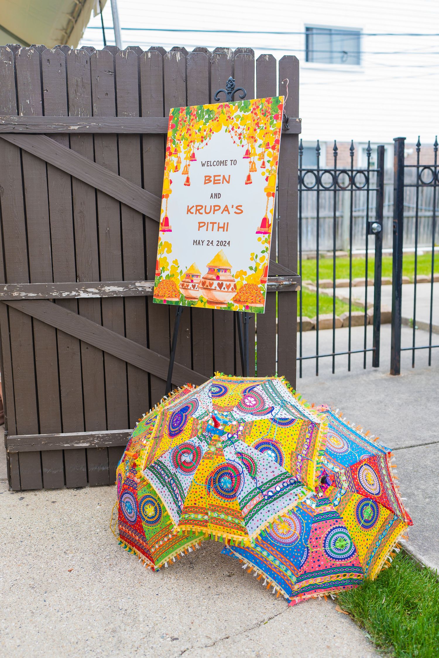 Colorful Indian wedding decor with decorated umbrella and event sign on wooden fence.