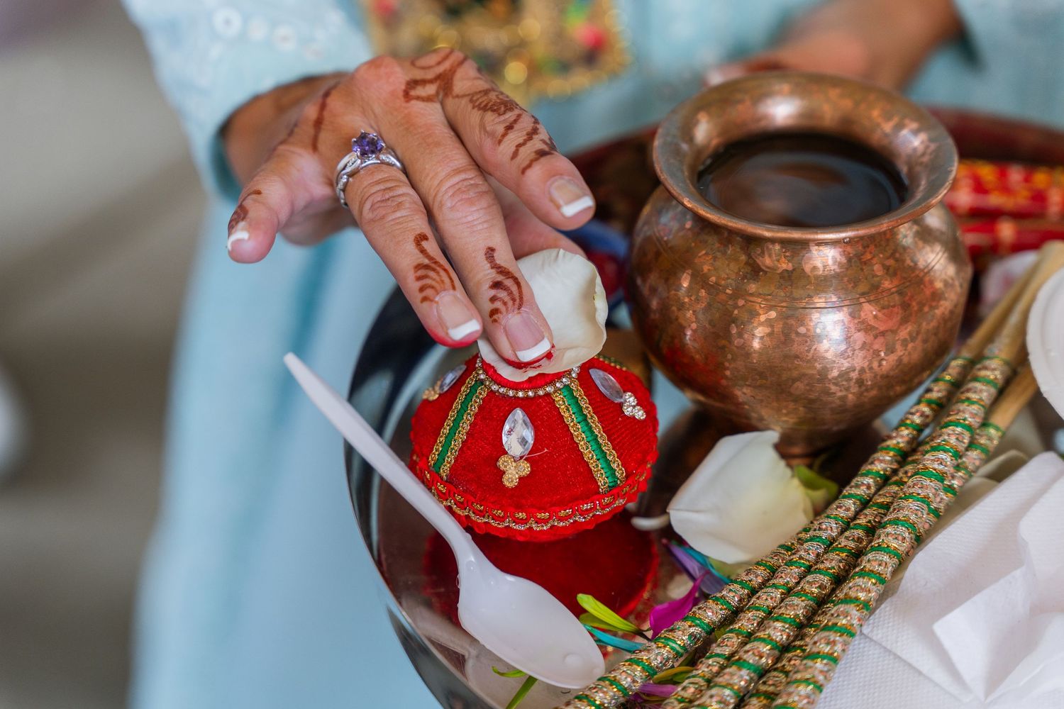 Close-up of decorated hands performing traditional Indian wedding ritual with ornate vessels.