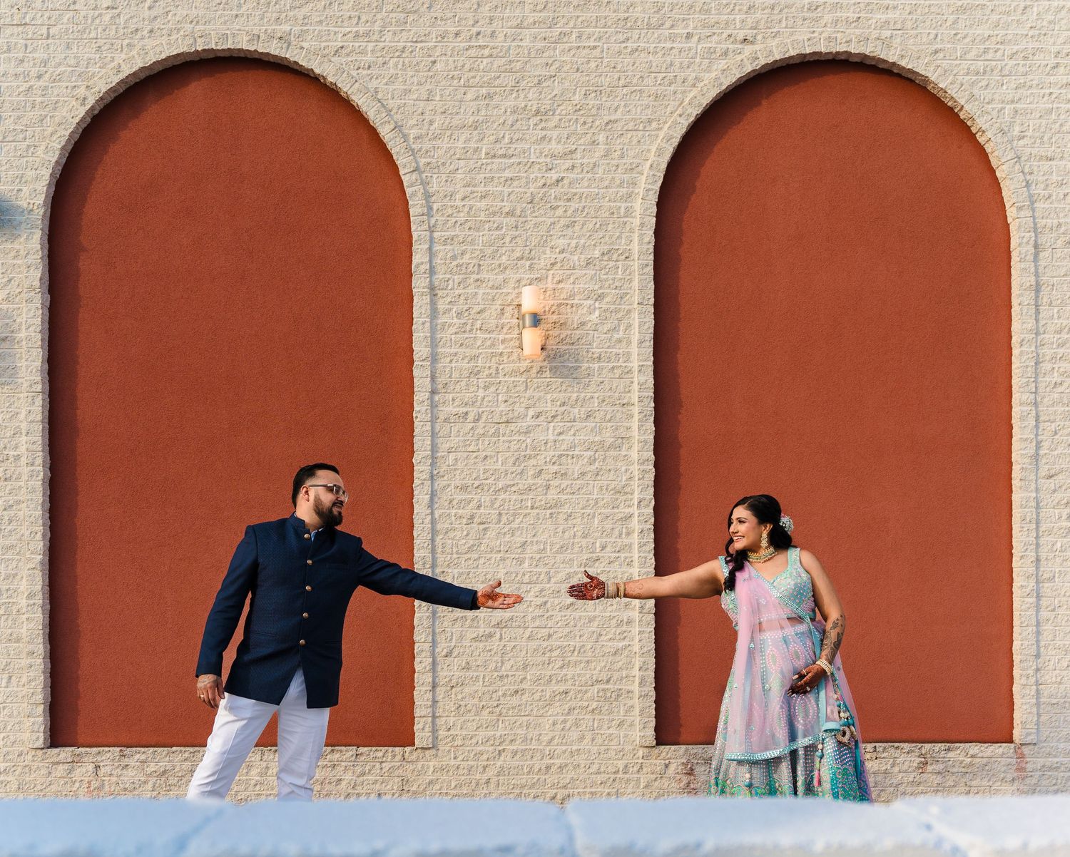 A couple reaches towards each other while standing in separate terracotta archways.
