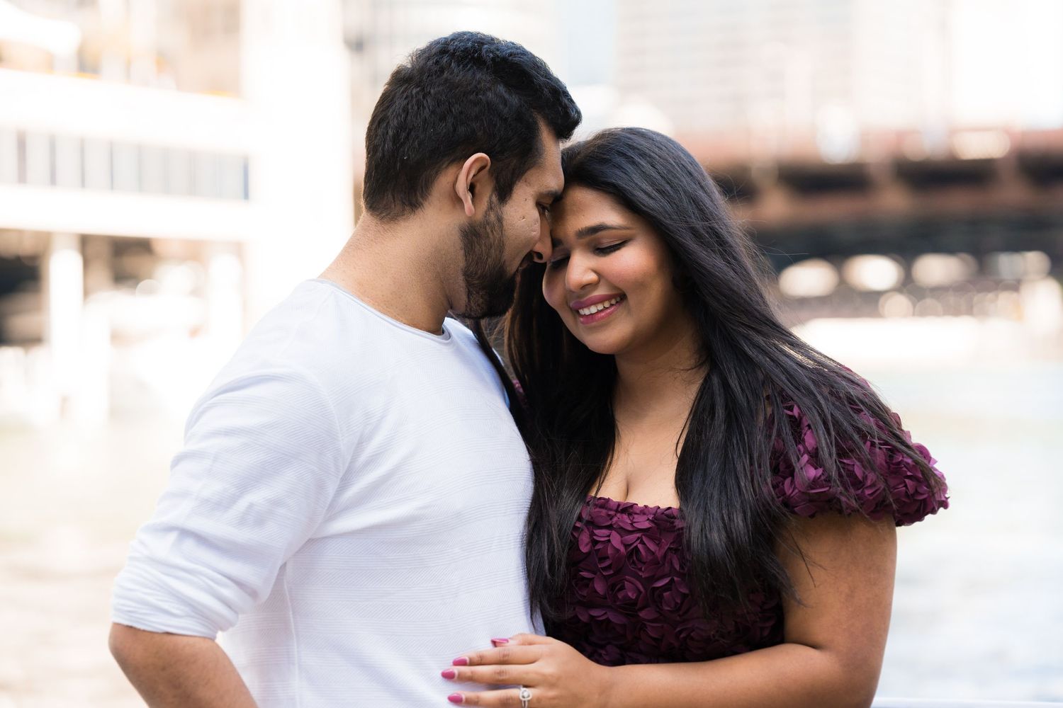 Romantic engagement photo of couple in burgundy and violet outfits sharing a tender moment.
