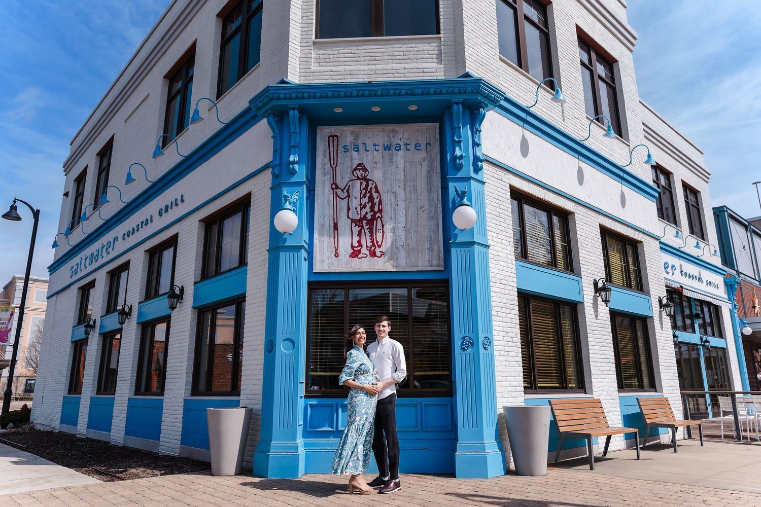 A couple embraces outside a bright blue and white corner restaurant building on a sunny day.