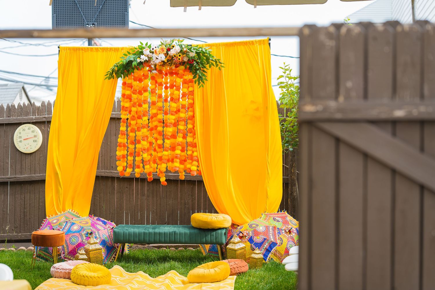 Yellow fabric backdrop with orange flower garlands creating traditional Indian wedding mandap.