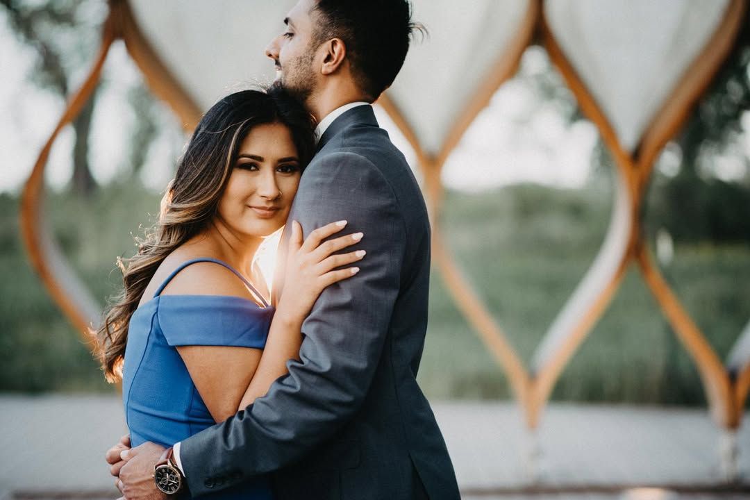 A couple in formal attire embracing against a geometric patterned background.