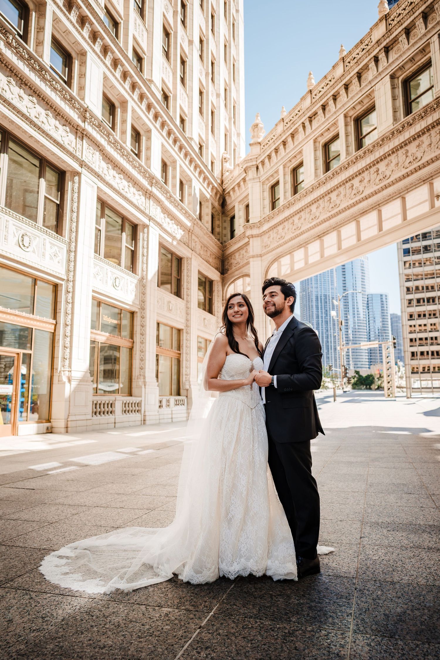 Bride and groom posing in front of an ornate historic building in an urban cityscape on their wedding day.