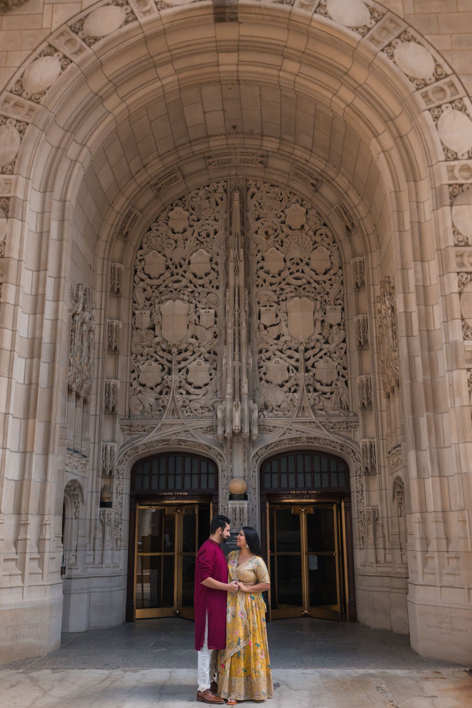 A couple poses beneath an ornate stone archway with detailed Gothic architectural elements.