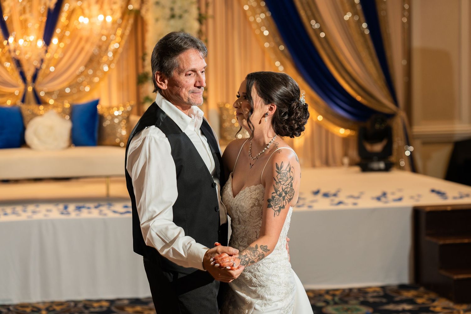 Couple dancing and laughing together at their wedding reception with draped backdrop and twinkle lights.