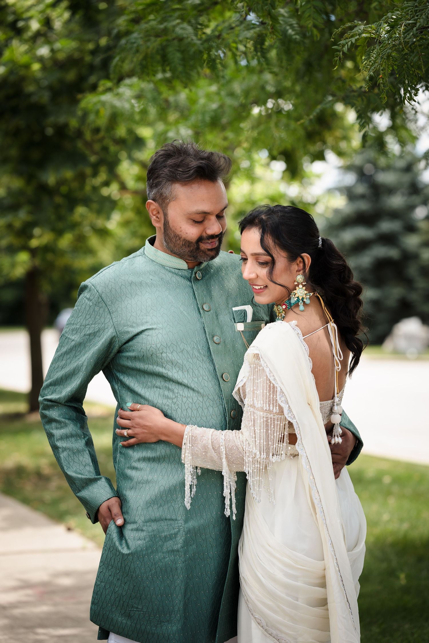 A couple embraces in traditional South Asian wedding attire in a garden setting.