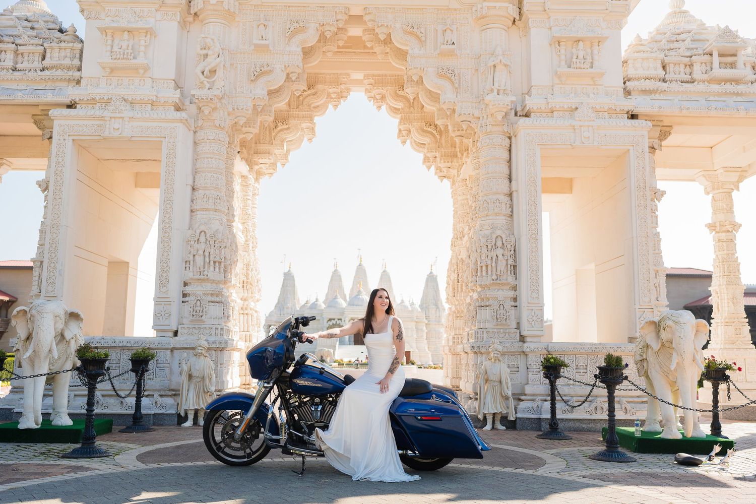 Bride posing with blue Harley Davidson motorcycle at ornate white temple architecture.