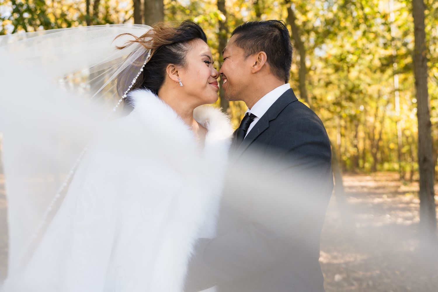A romantic wedding portrait of a couple sharing an intimate moment in a sunlit outdoor setting.