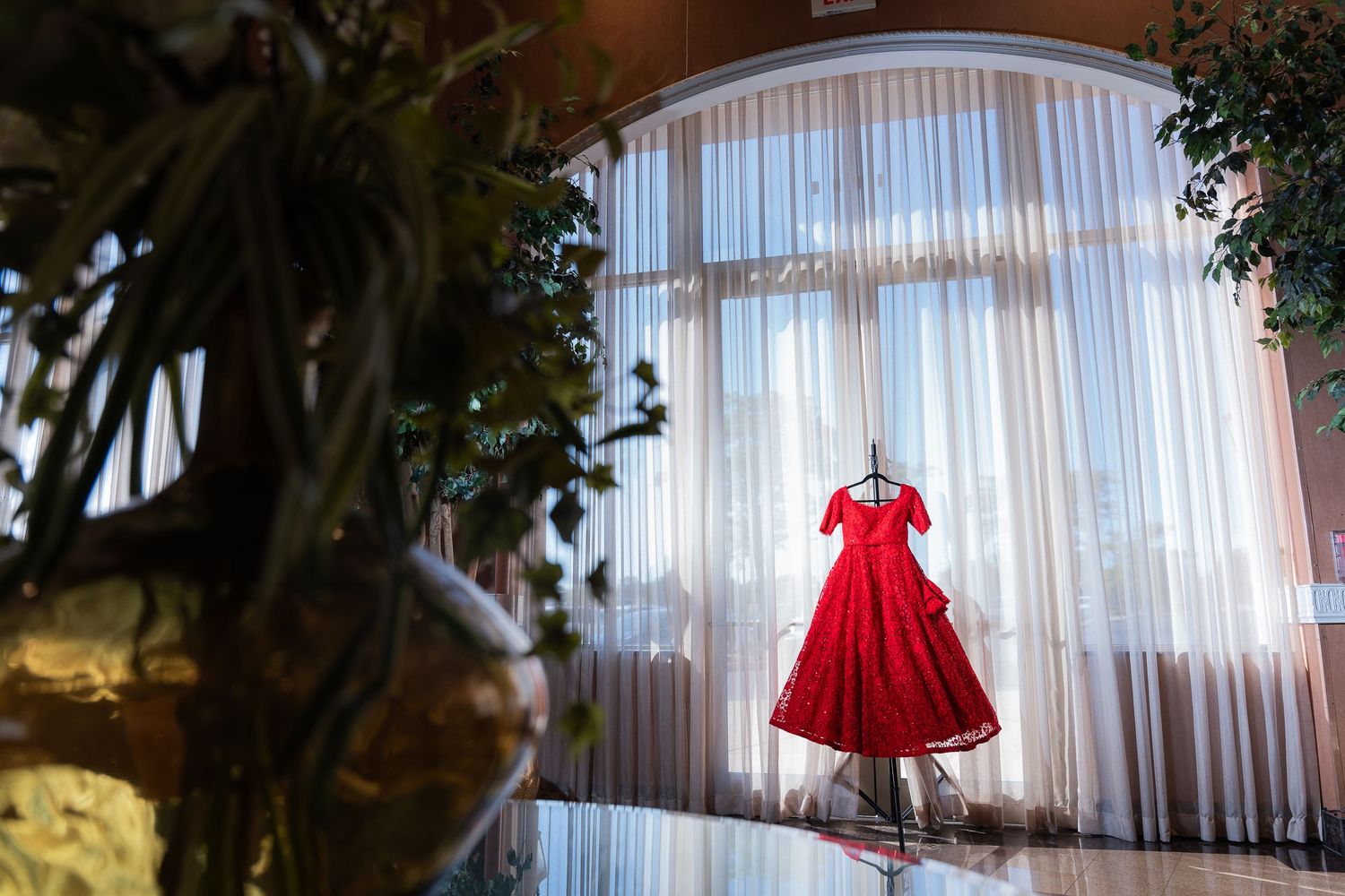 Red wedding dress displayed elegantly against white curtained backdrop in natural lighting.