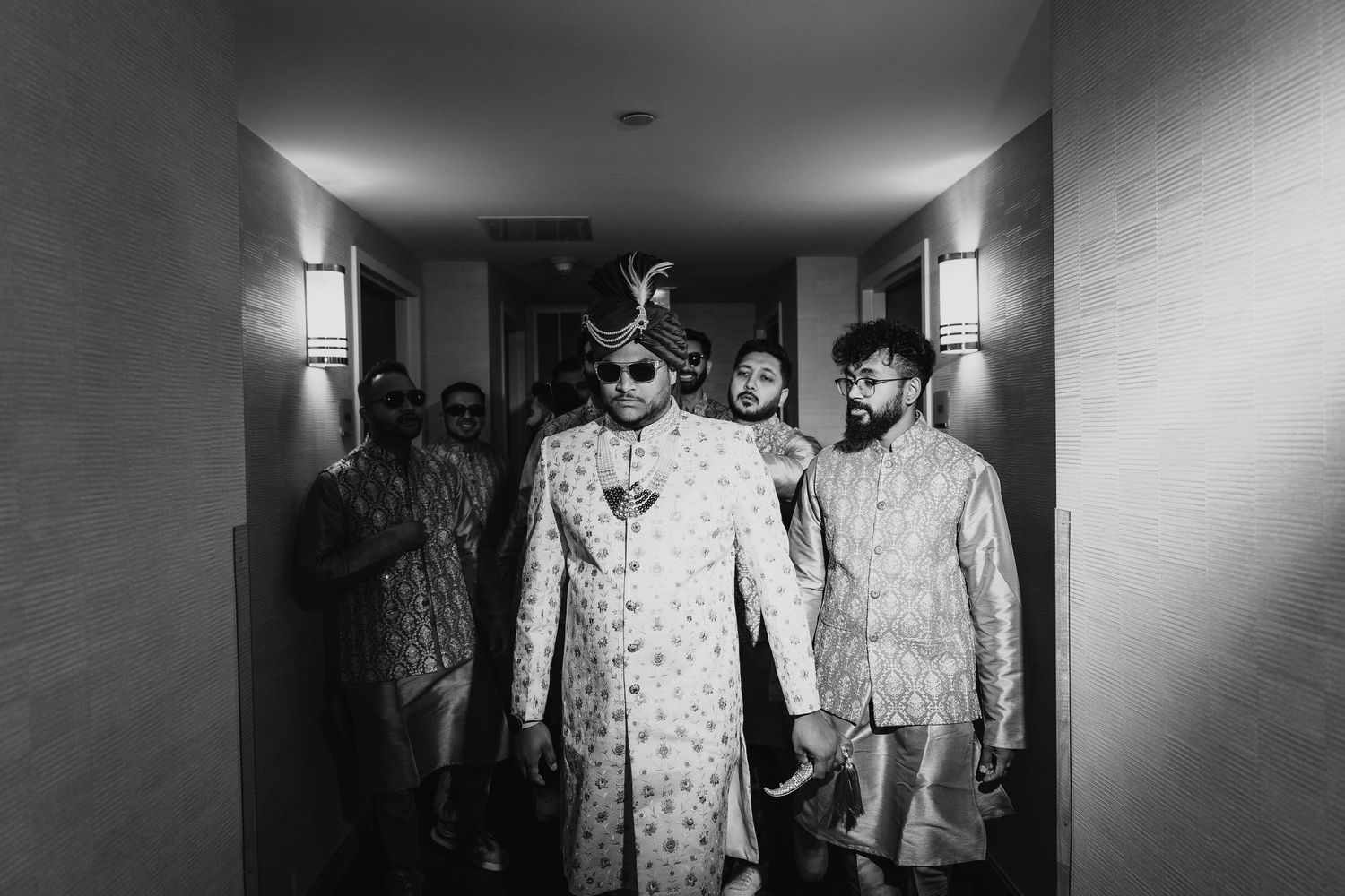 Wedding party walking down hotel hallway in traditional South Asian formal wear.