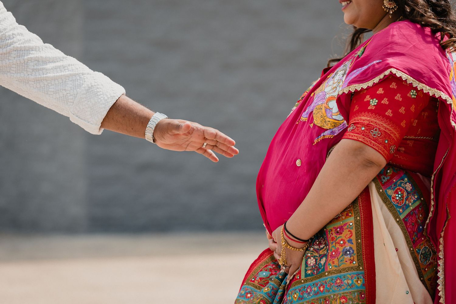 Detail shot of traditional Indian wedding attire with intricate embroidery and reaching hands.