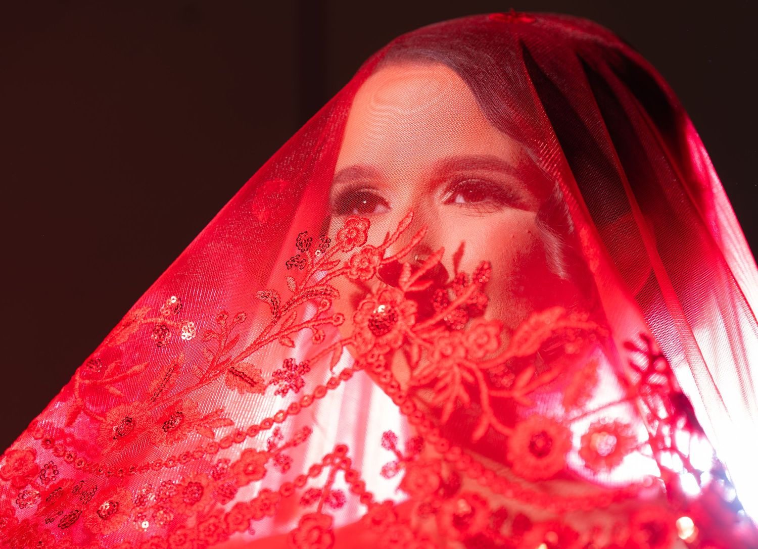 Red lace veil creating a dramatic effect with vibrant lighting in a wedding photography shot.