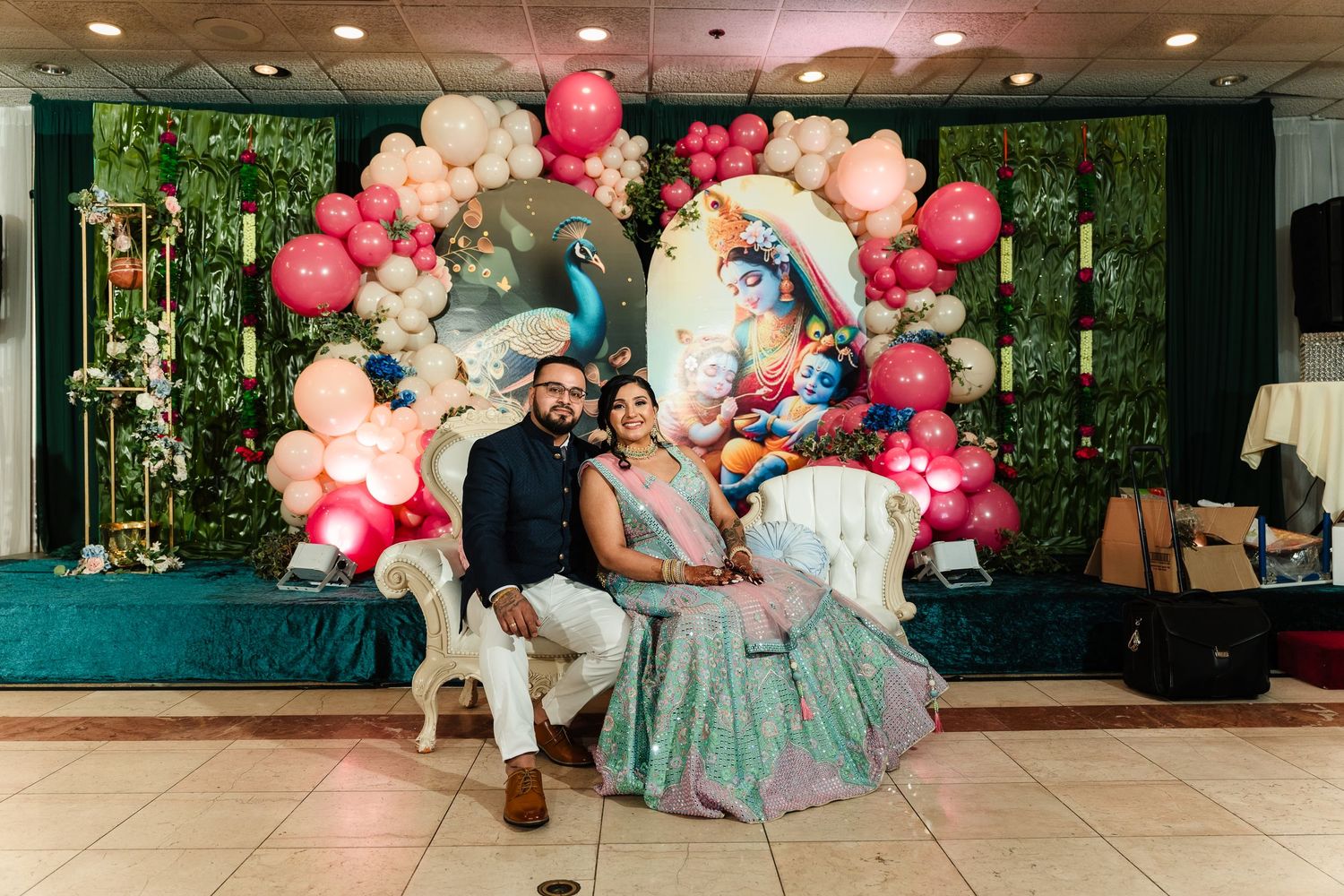 Couple seated under elaborate balloon arch with pink and white decorations at reception.
