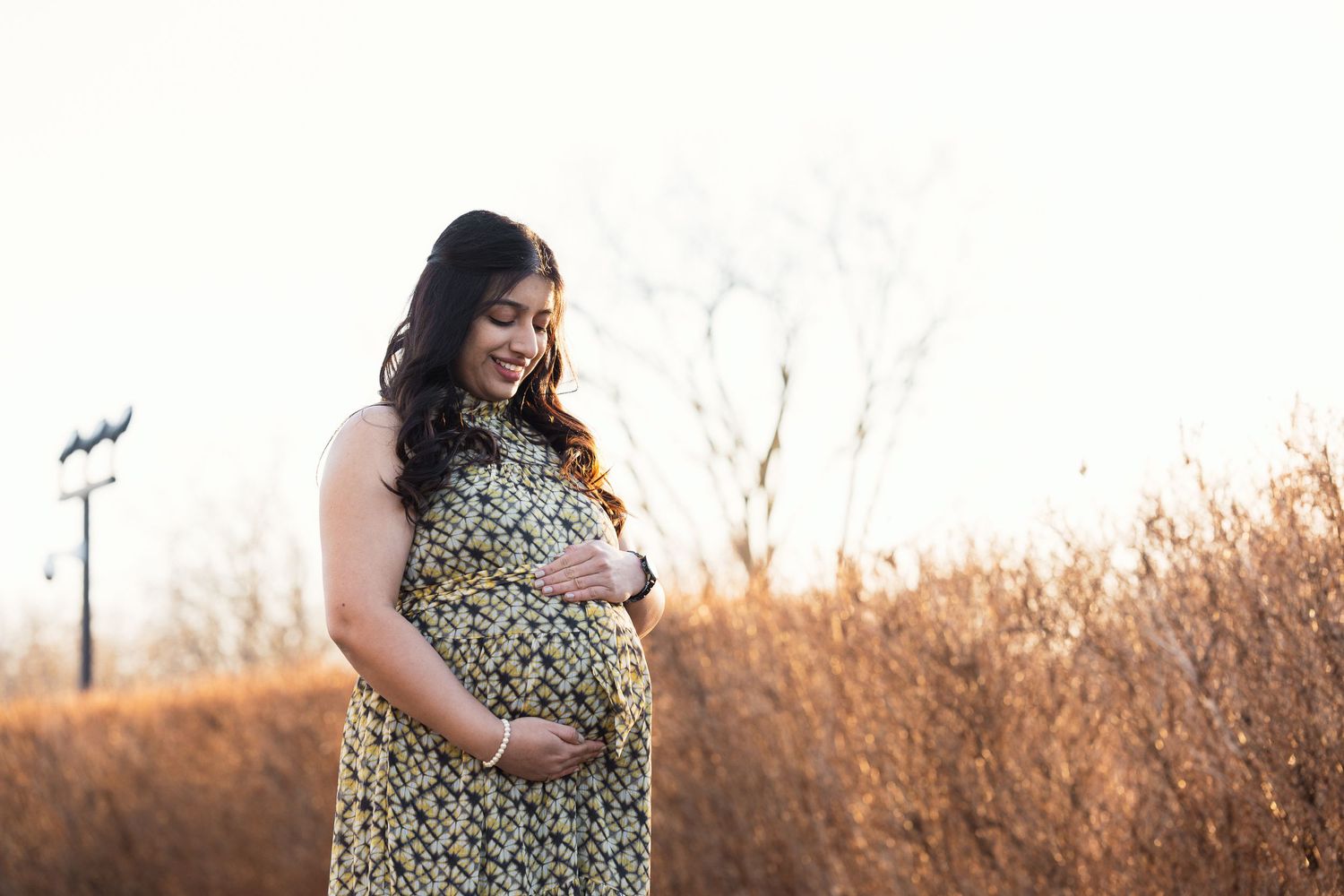 Expecting mother in floral dress smiles during outdoor autumn maternity session.
