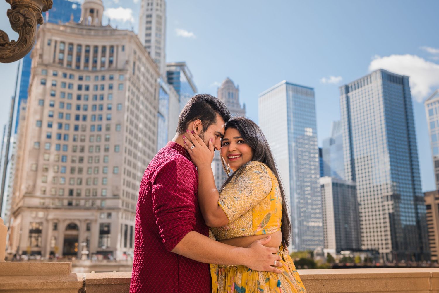 Couple in traditional Indian attire embracing against Chicago skyline backdrop.