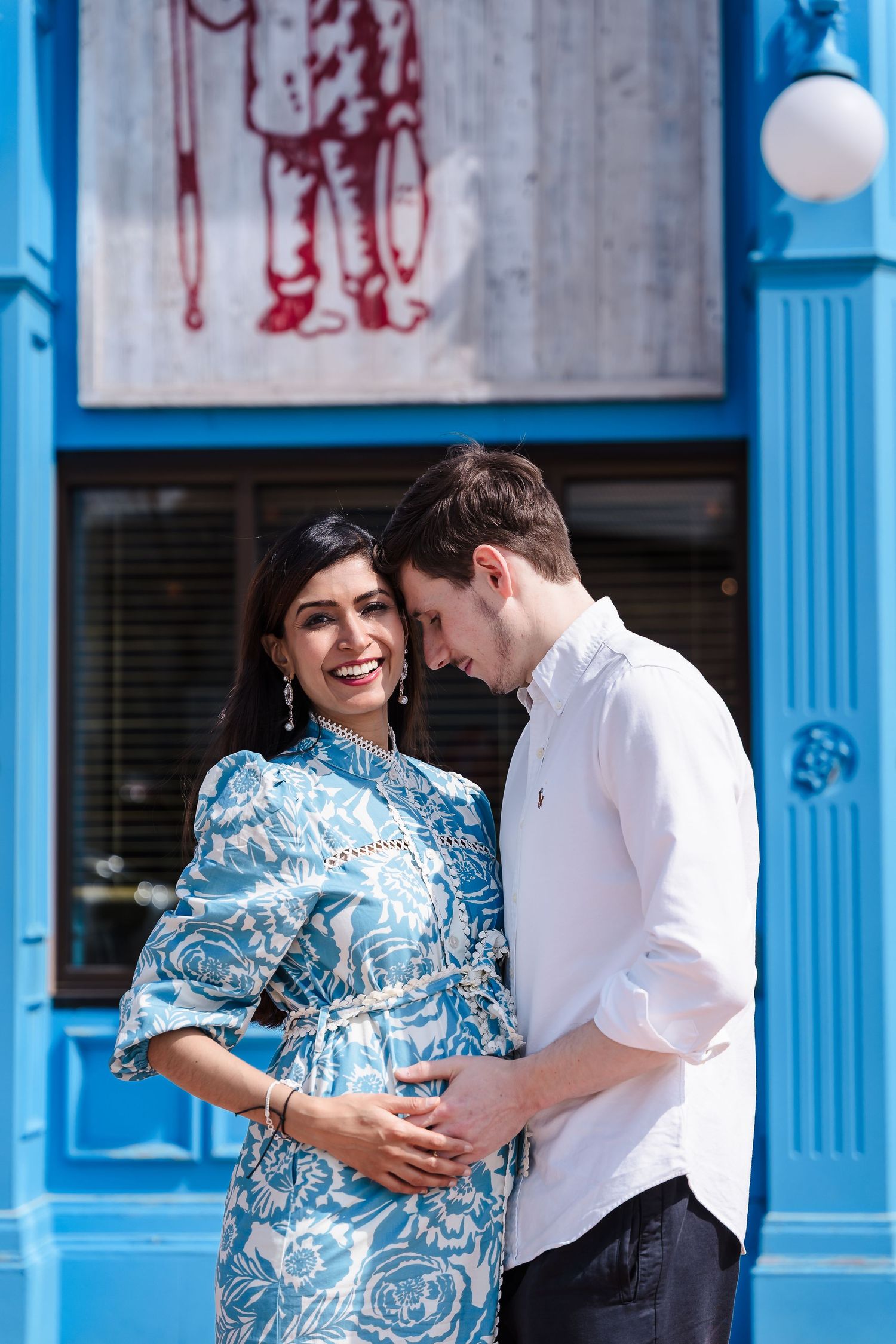 A couple shares an intimate moment together against a bright blue storefront on a sunny day.