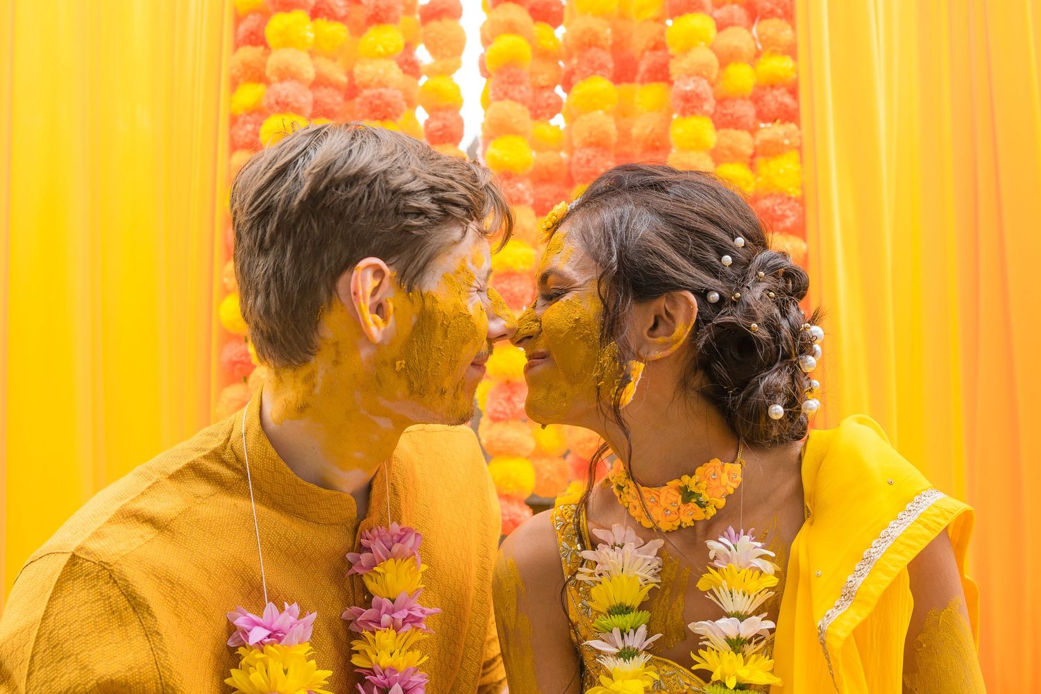 Intimate moment between couple during haldi ceremony with yellow backdrop and flower garlands.