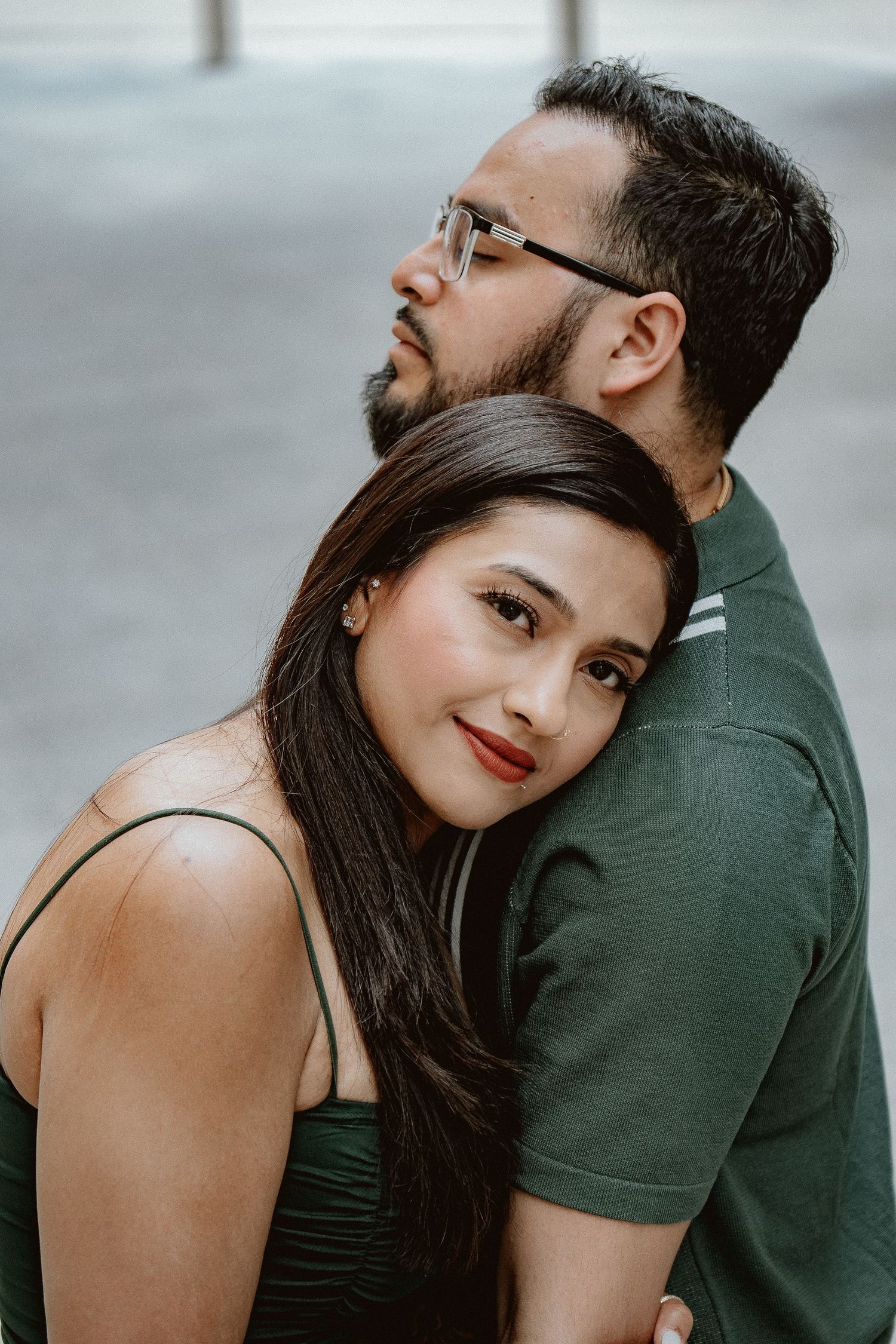 A couple poses intimately against a blurred background in casual attire.