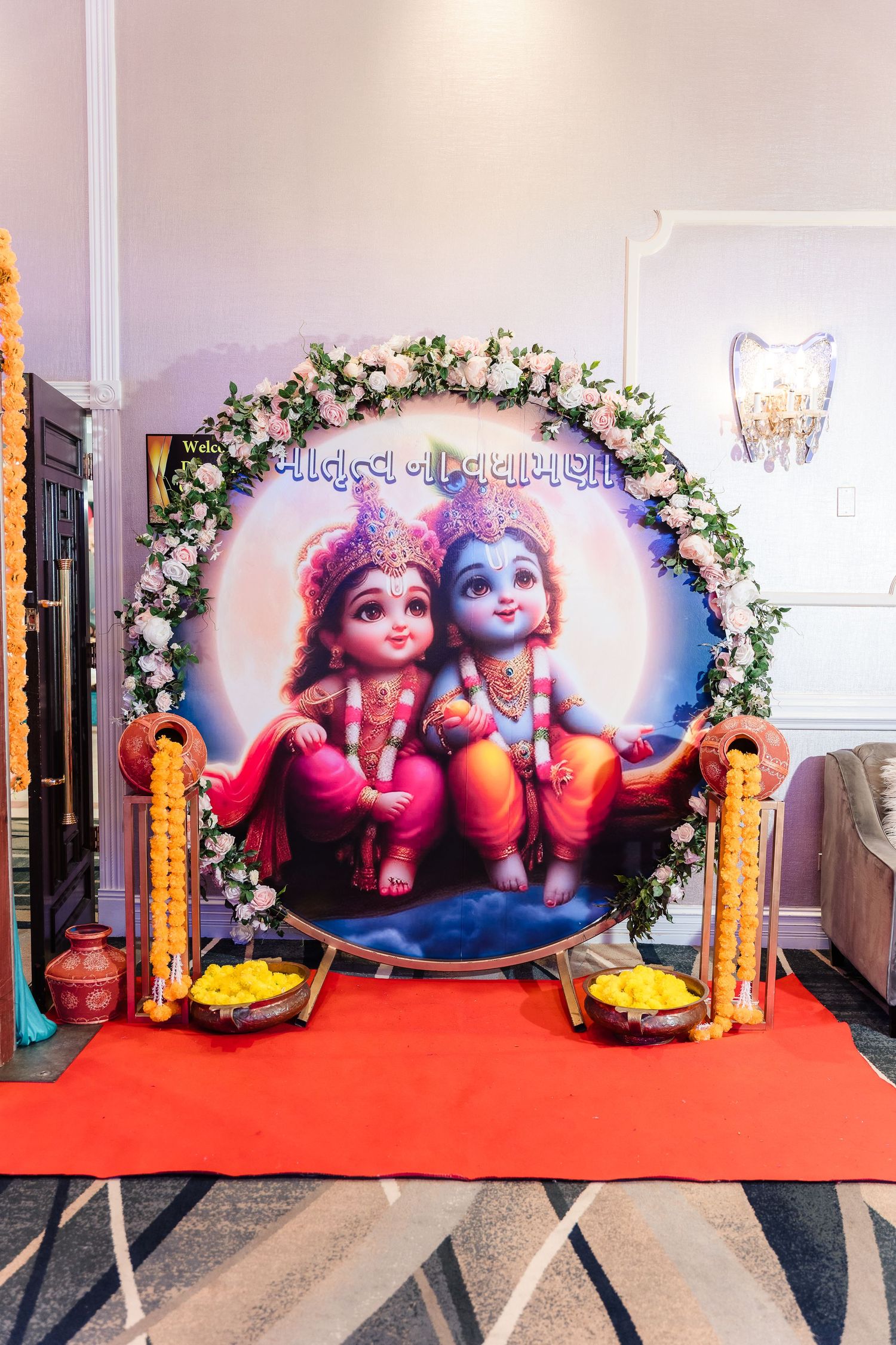 Decorative arch with floral design featuring Krishna artwork and traditional Indian elements on red carpet.