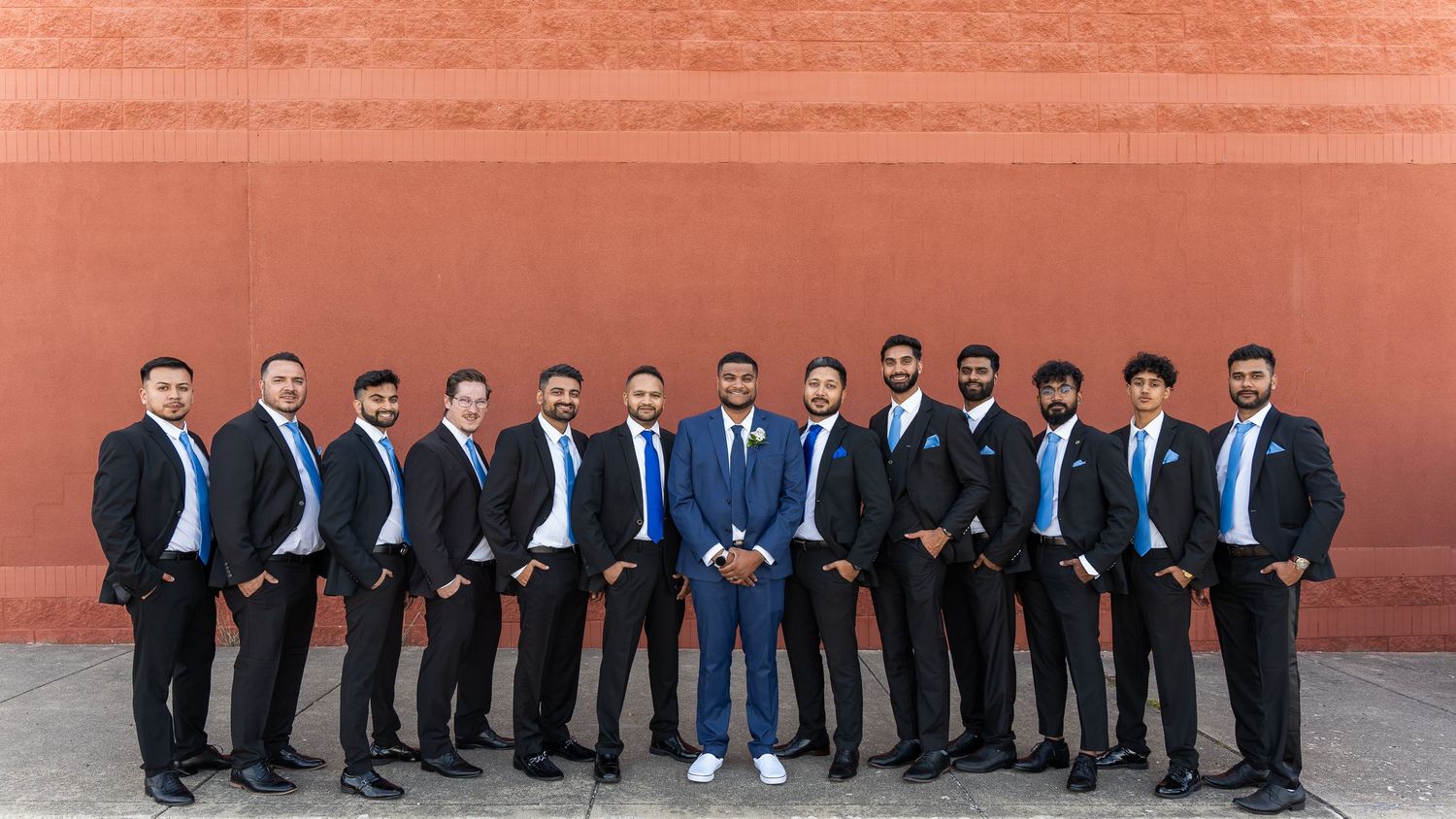 Groomsmen in dark suits and blue ties pose against terra cotta wall.