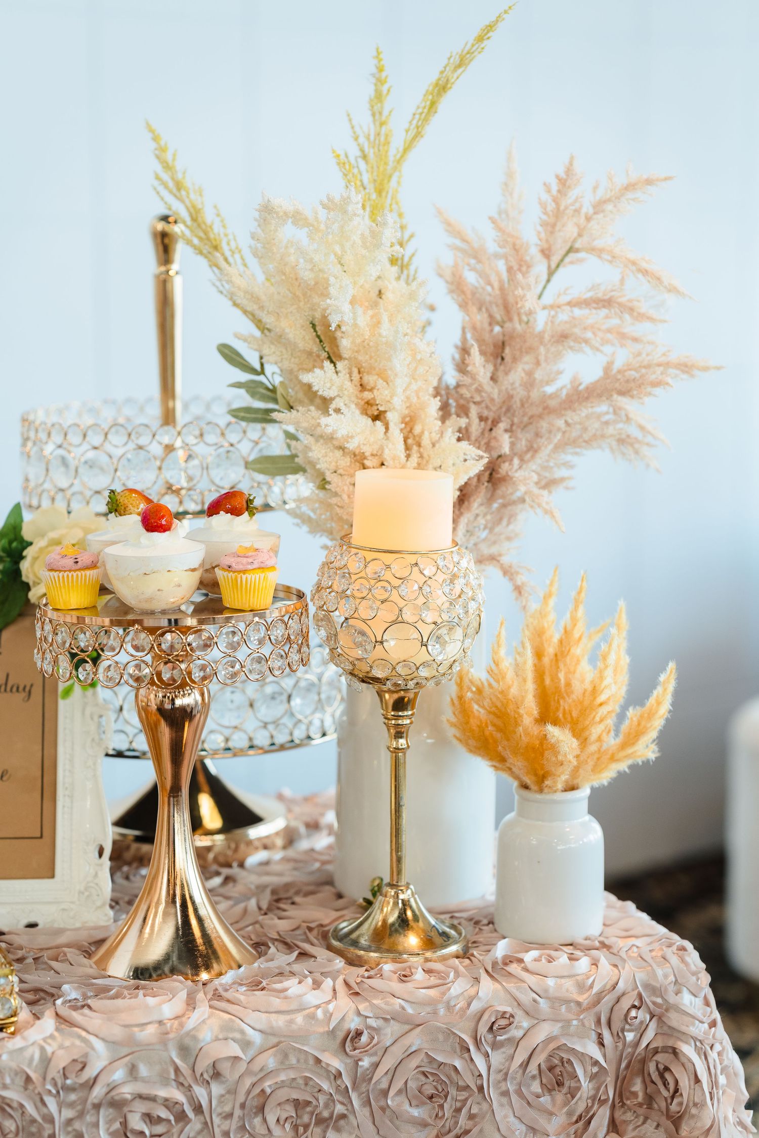 Elegant dessert display with pampas grass decor and gold cake stands on a rose-patterned tablecloth.