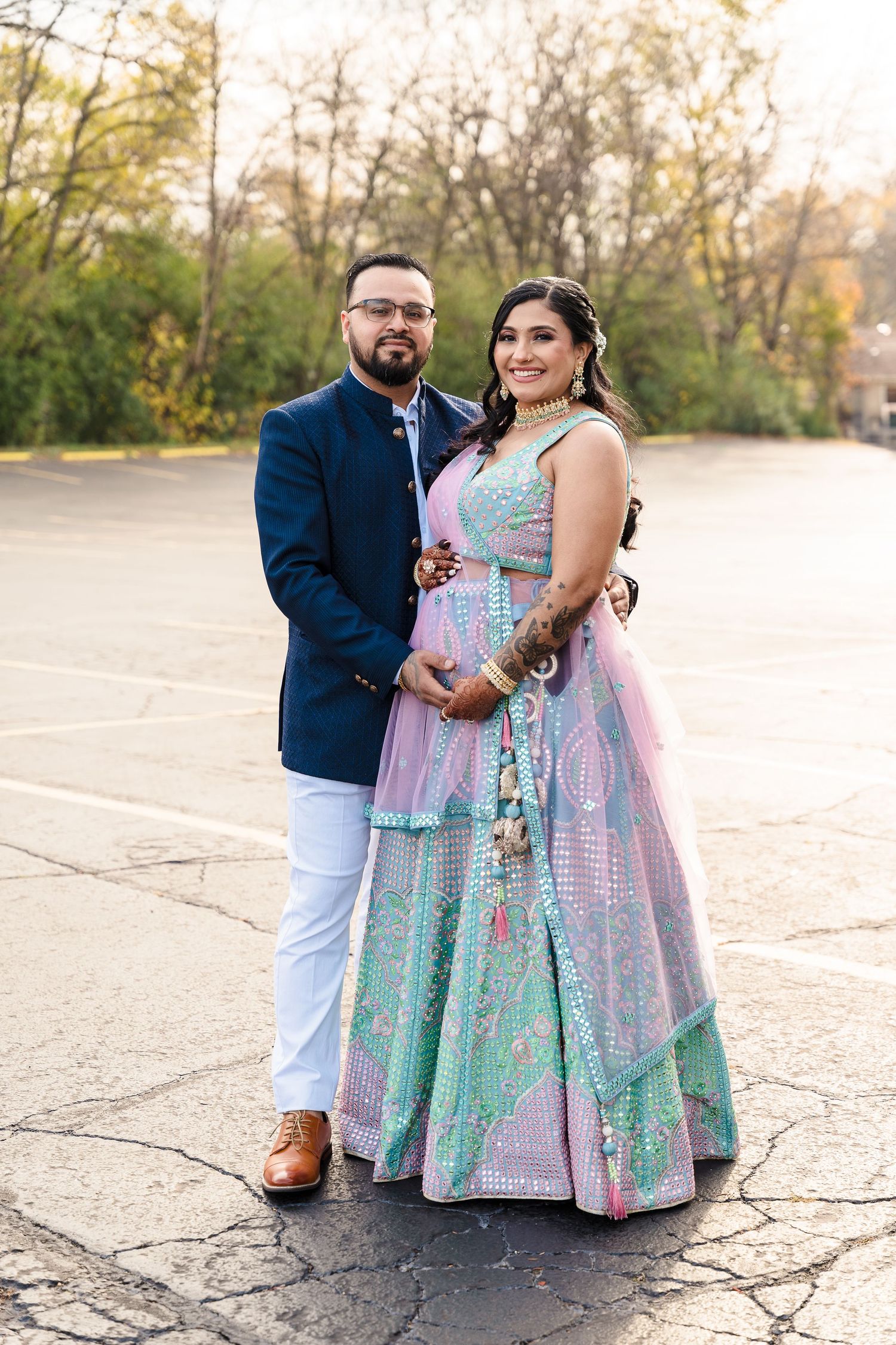 A couple poses outdoors wearing traditional Indian fusion attire with a navy blazer and mint lehenga dress.