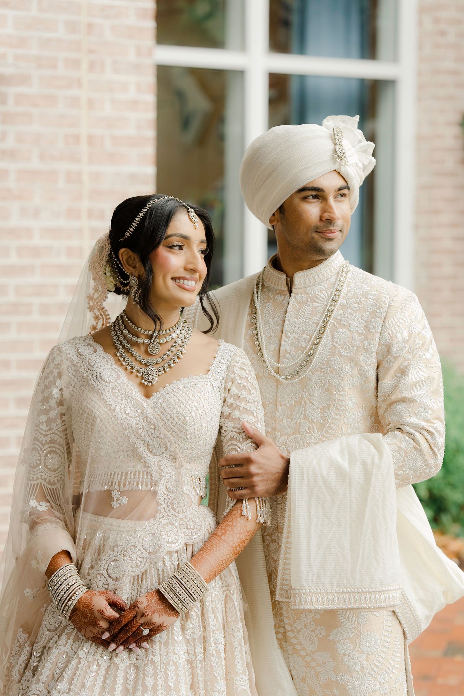 South Asian bride and groom in matching ivory embroidered wedding attire, bridal lehenga and sherwani with turban.