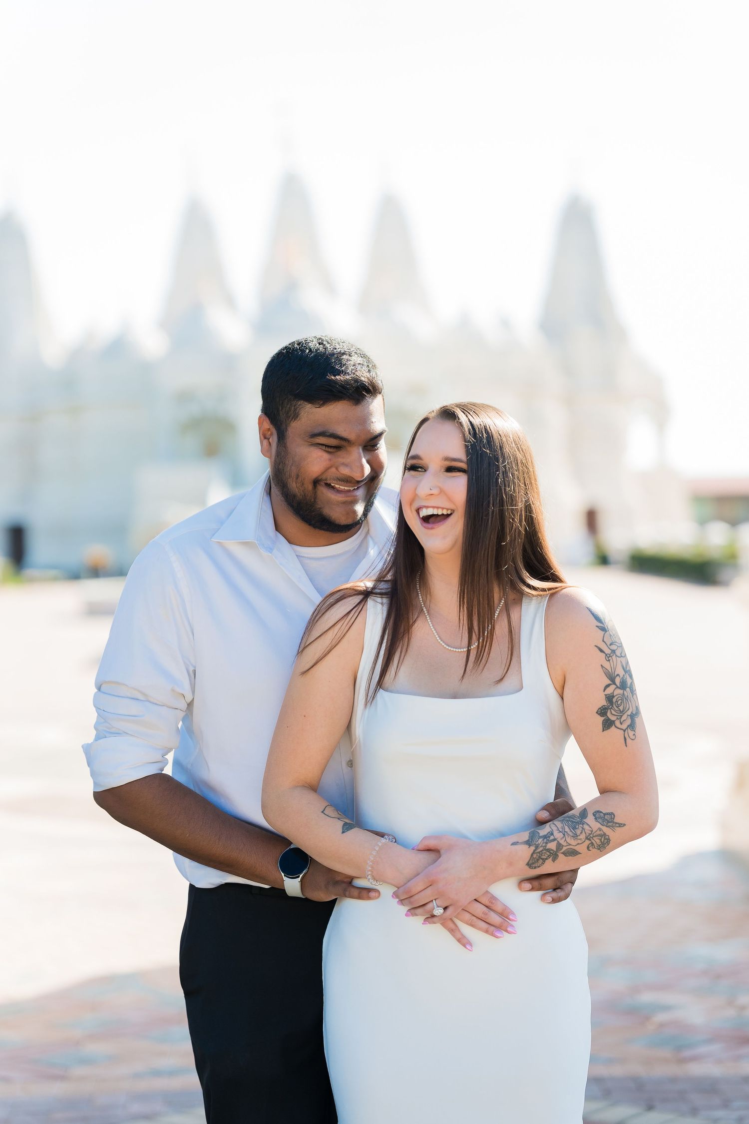 Happy couple embracing and laughing during their outdoor photoshoot with architectural backdrop.