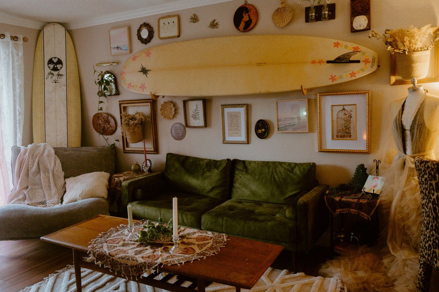 Cozy living room with green velvet sofa, surfboard wall decor, framed art, and wooden coffee table on patterned rug.