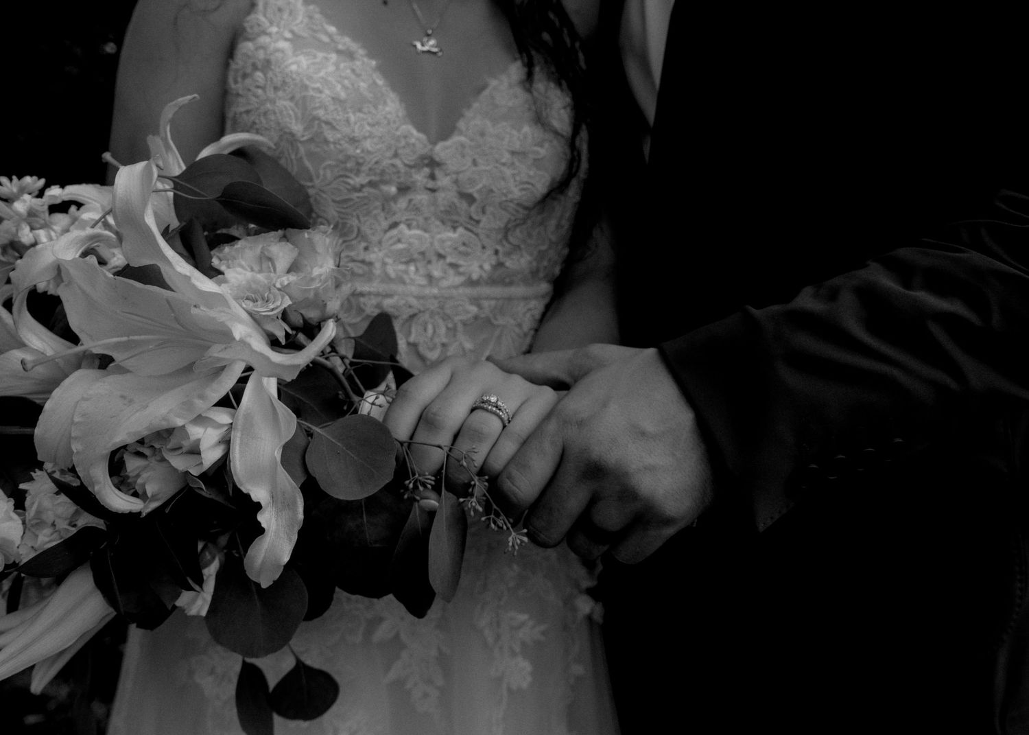Black and white close-up of a bride holding a bouquet while a groom holds her hand.