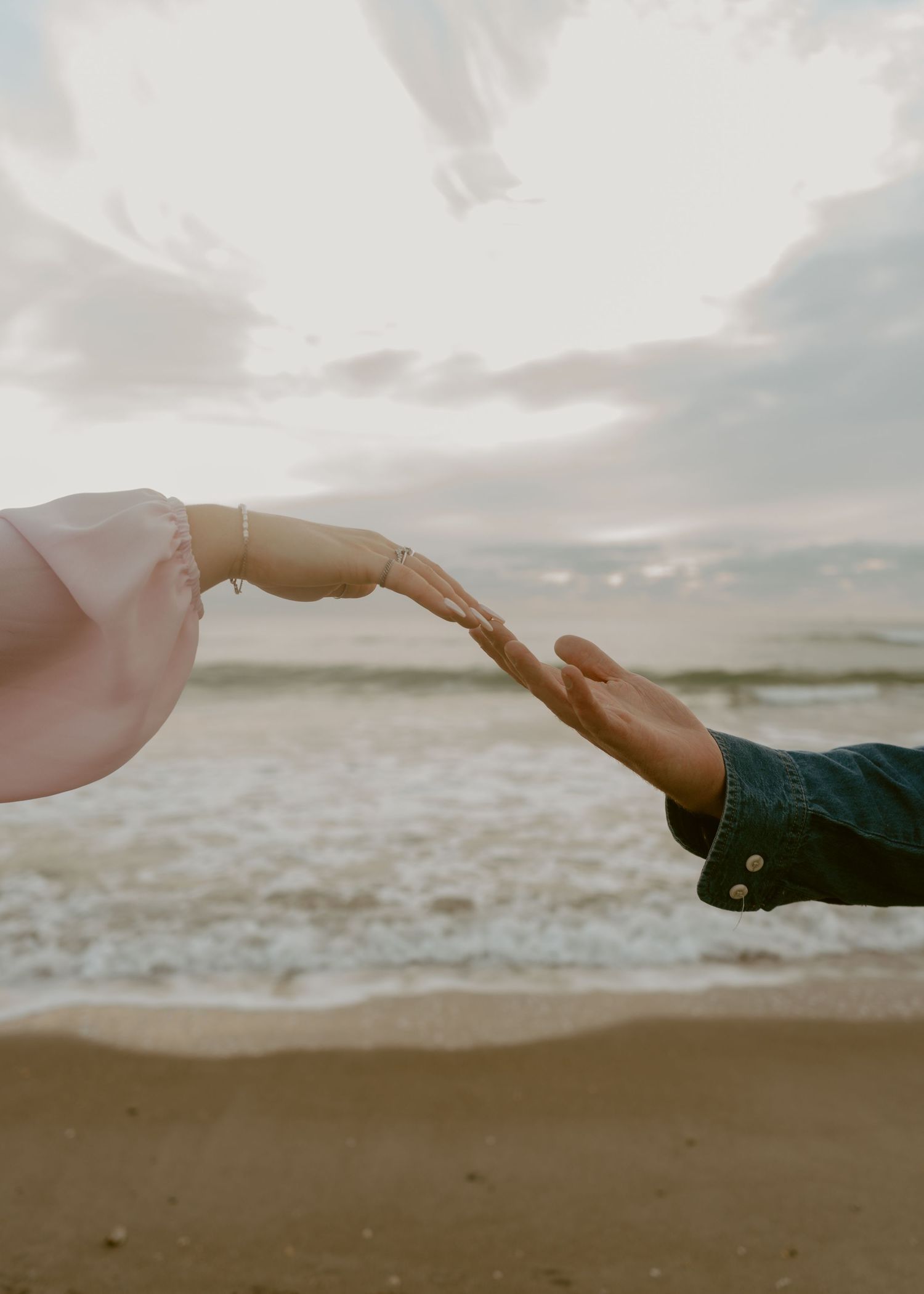 Couple reaching hands toward each other on sandy beach at golden hour sunset.