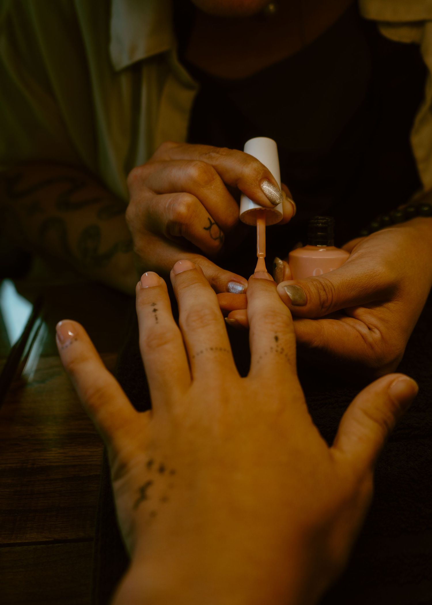 Close-up of a person applying nude pink nail polish to another person's hand indoors.