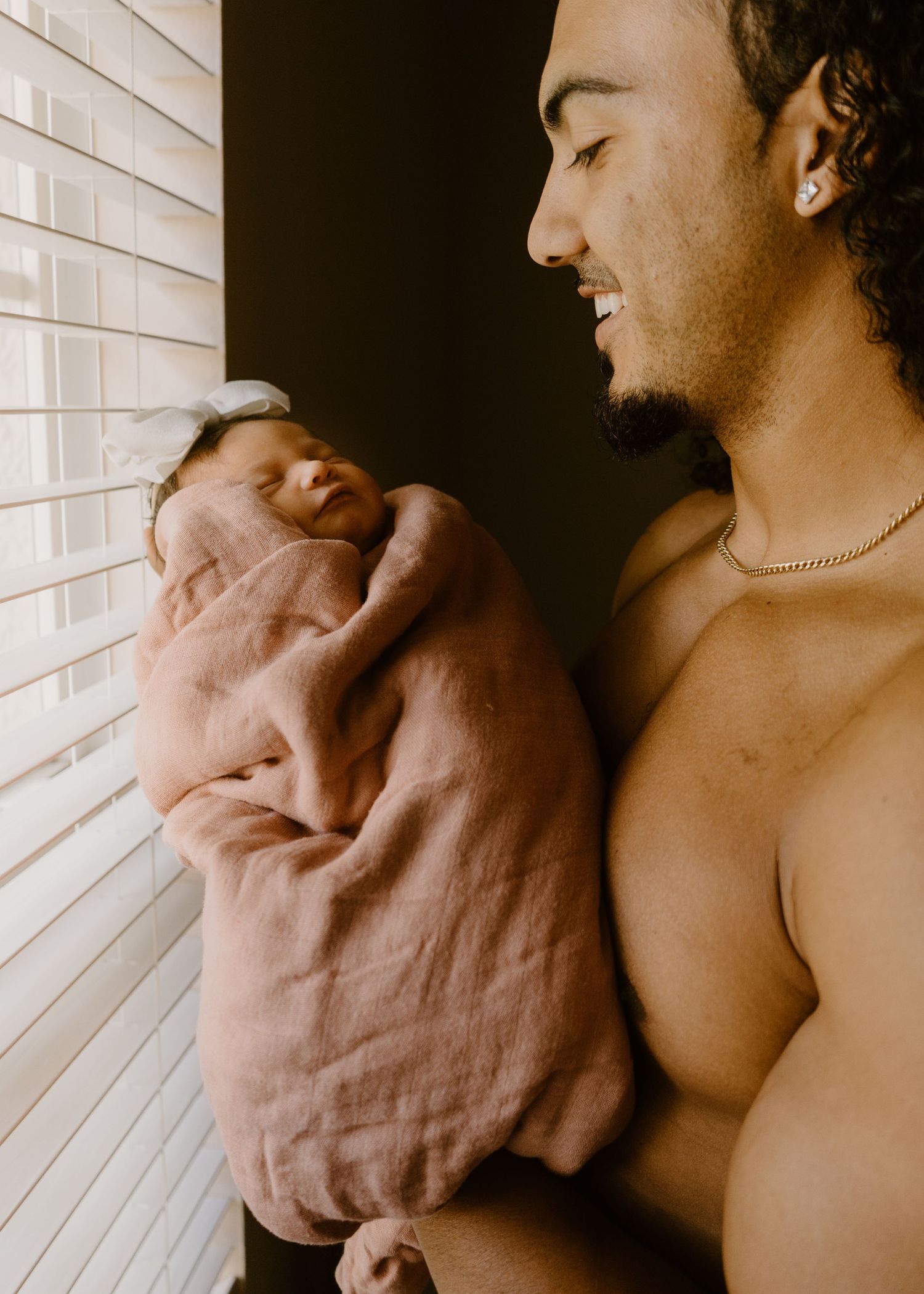 Smiling father tenderly holding swaddled newborn baby by a sunlit window.