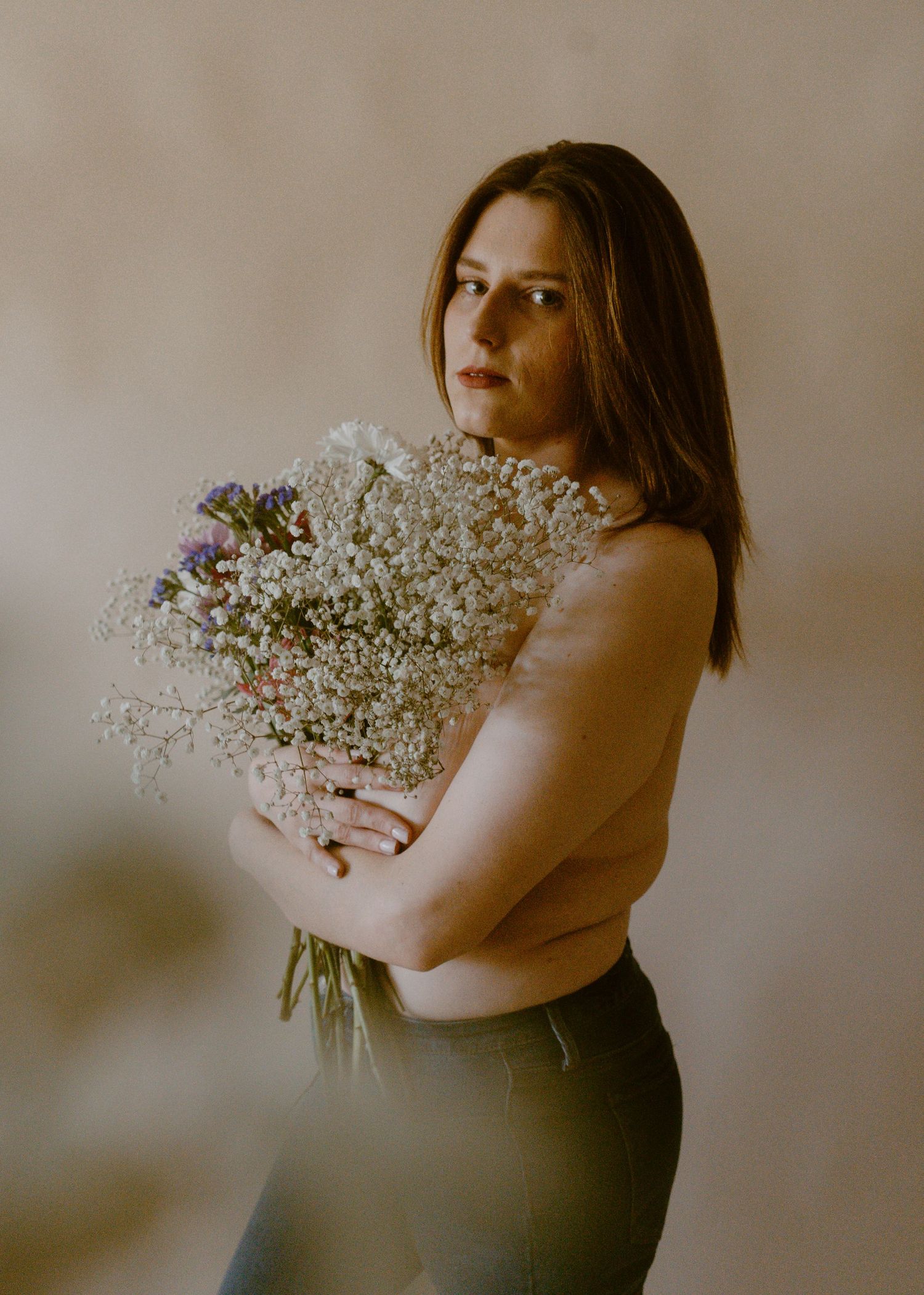Woman holding large bouquet of white baby's breath flowers against neutral background.