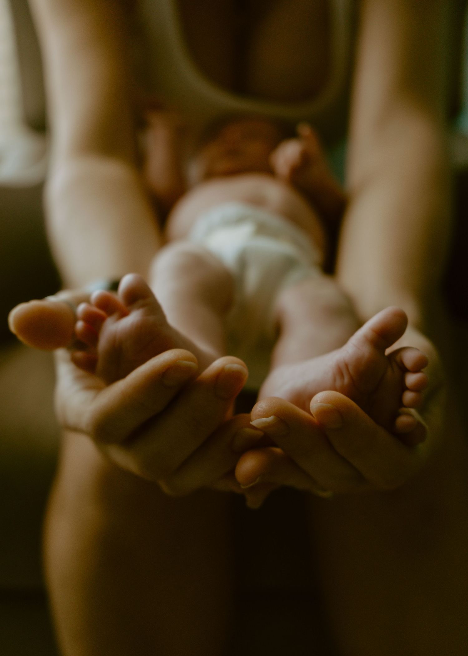 A mother gently cradles her newborn baby's tiny feet in her cupped hands in a tender close-up photo.