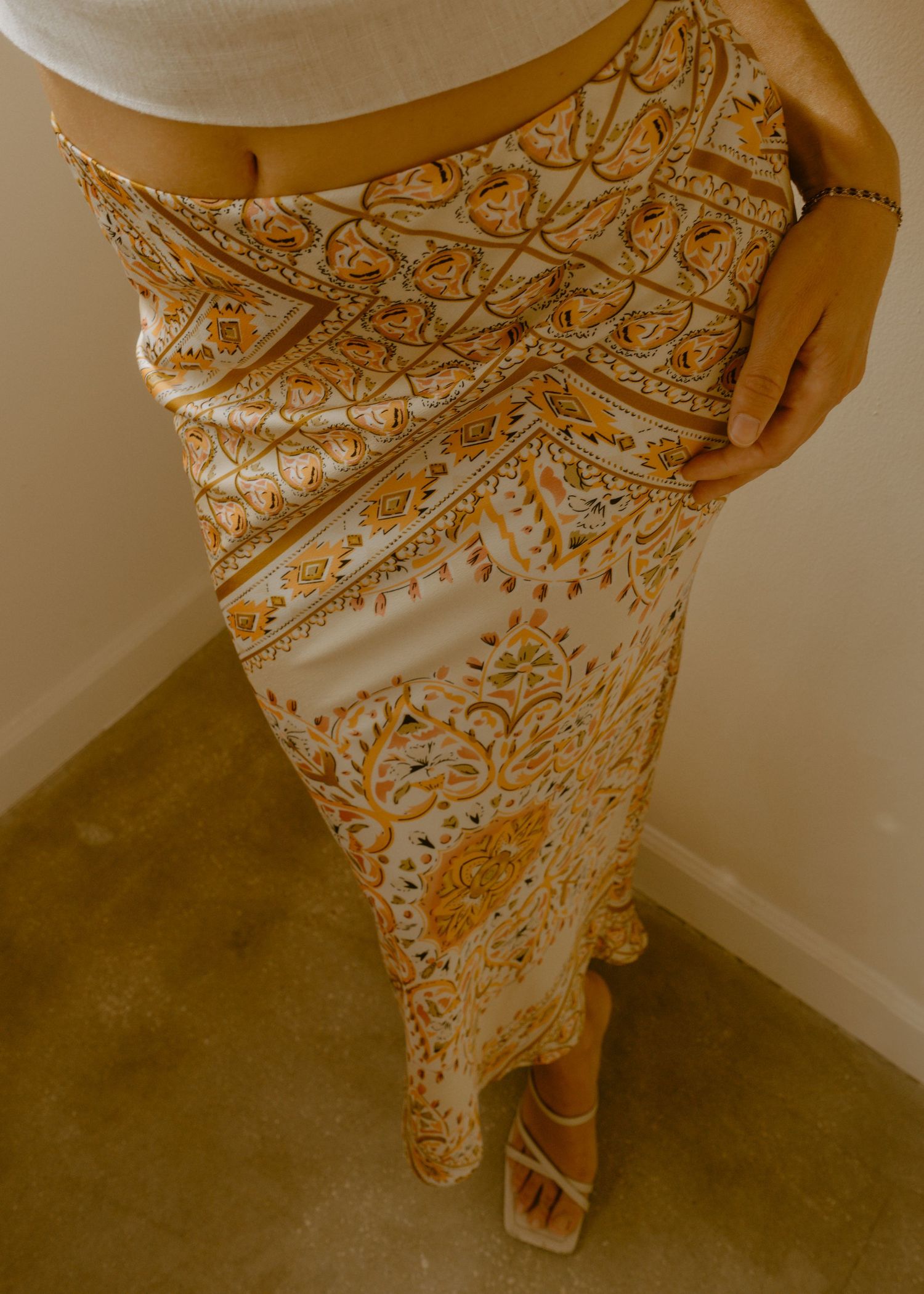 Woman wearing a white and gold paisley print maxi skirt with white strappy heels.