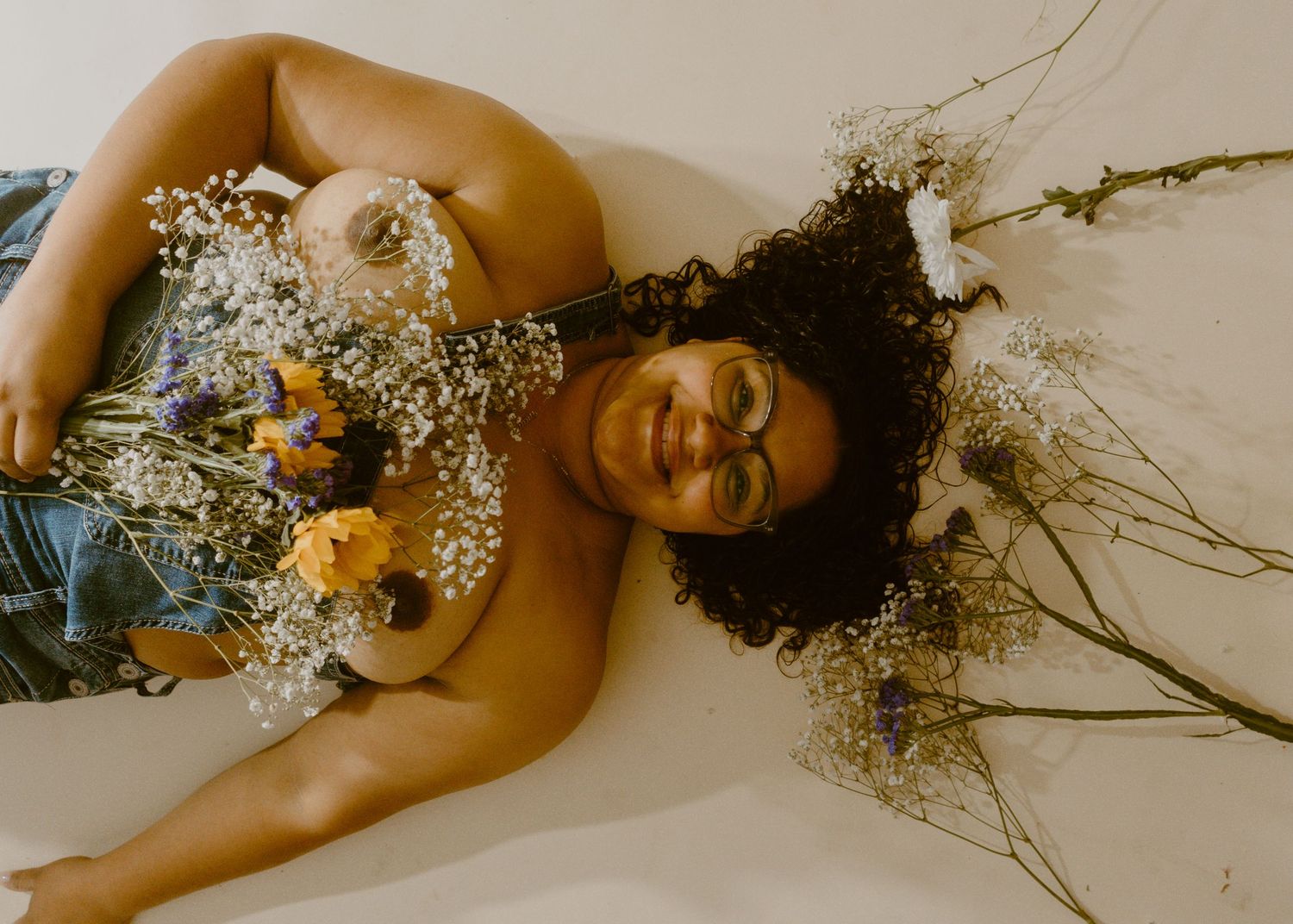 Person lying down surrounded by colorful wildflowers and baby's breath in their hair, smiling serenely.